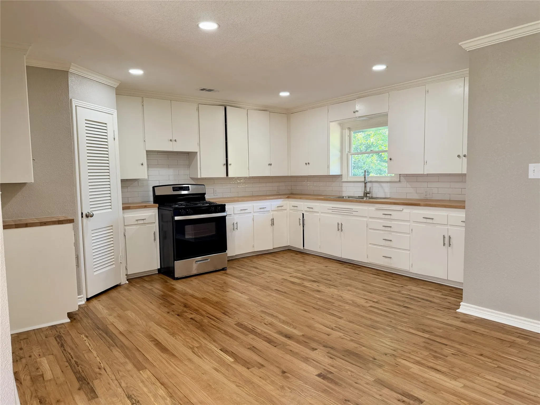 Bright, updated kitchen featuring white cabinetry, stainless steel appliances, wood-finish flooring, subway tile backsplash, and recessed ceiling lighting