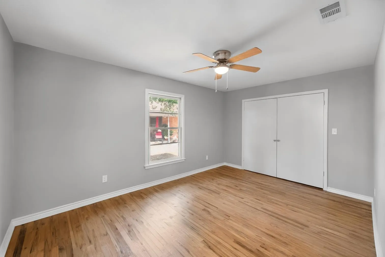 Wood-finish flooring, light gray walls, white trim, a single window, and a ceiling fan with integrated lighting
