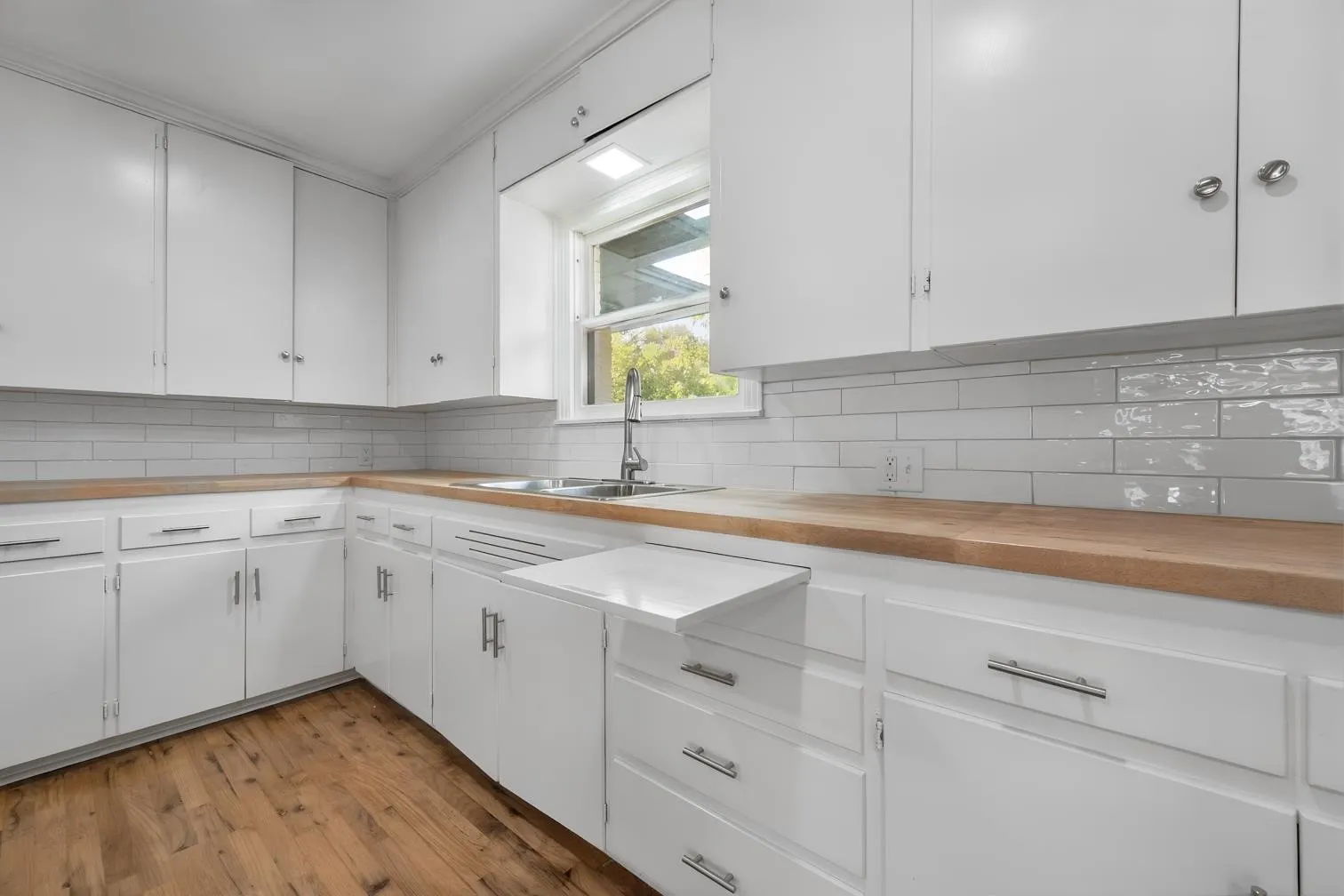 White cabinetry with brushed nickel hardware, wood-finish countertops, subway tile backsplash, and a stainless steel sink with a gooseneck faucet