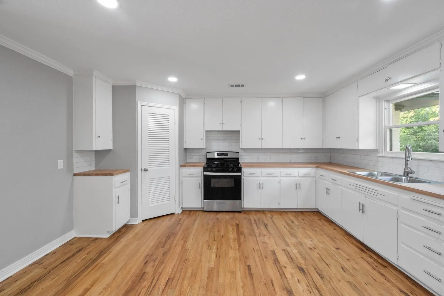 Well-appointed kitchen featuring hardwood flooring, white cabinetry, wood-finish countertops, stainless steel appliances, and a subway tile backsplash