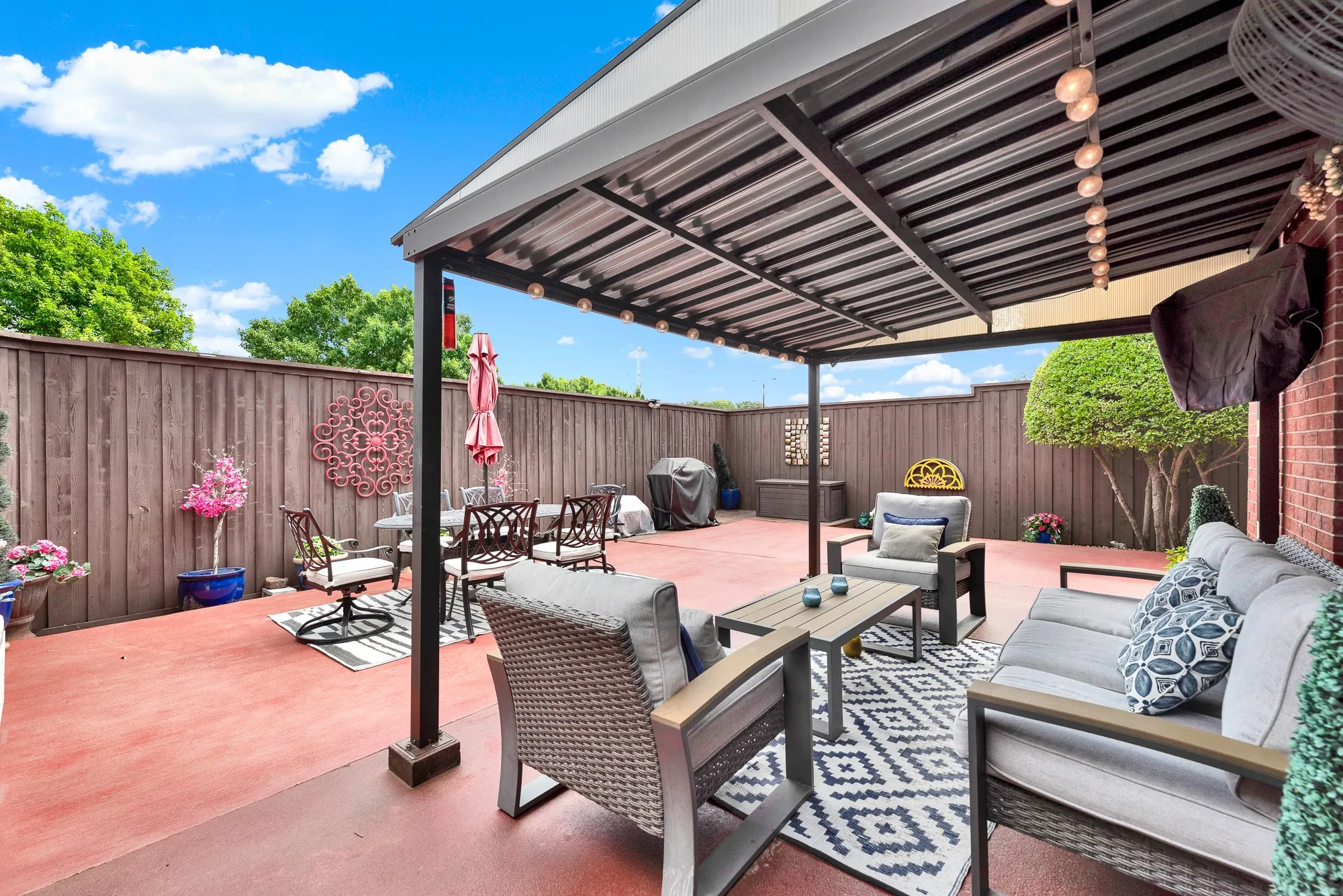 A covered pergola structure casts cool, filtered shade over the expansive patio floor. Picture unwinding outside after dinner as ambient string lights glow under the evening sky.