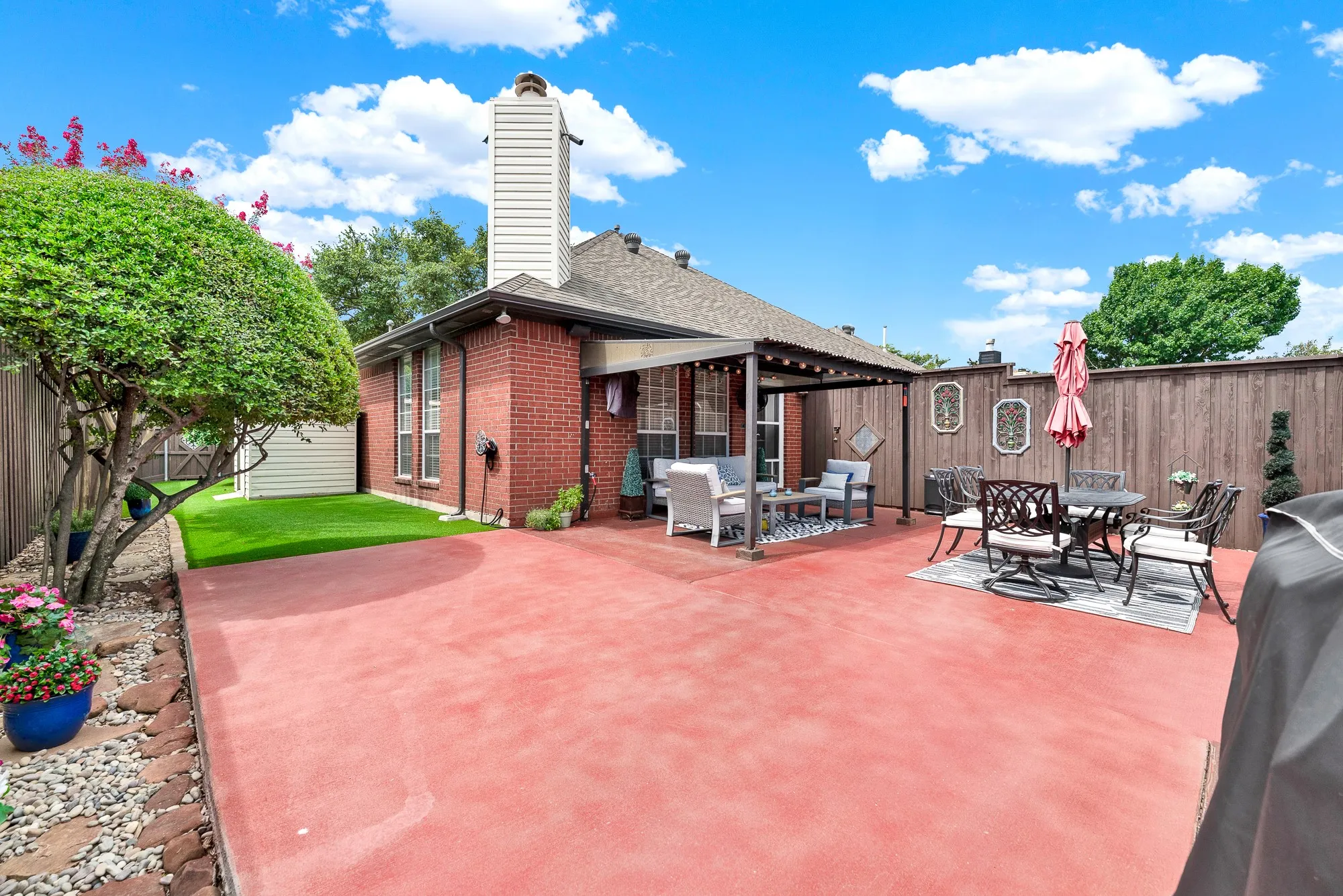 Lush artificial turf creates a vibrant green side lawn along the classic brick facade. Visualize pets or kids playing freely on pristine, worry-free grass all year round.