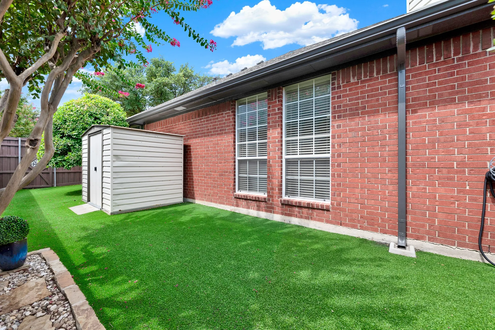 A neat exterior storage shed sits alongside large double-hung windows and vibrant green turf. Picture organizing seasonal lawn gear easily while enjoying a quiet, sunny morning outdoors.