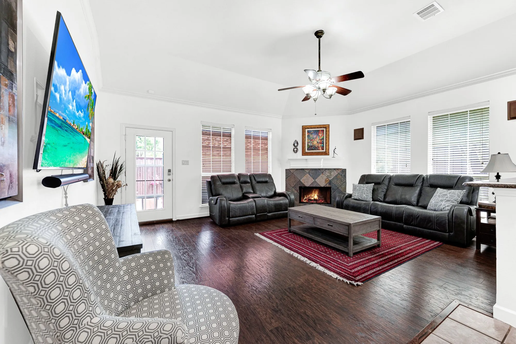 A corner-set tiled fireplace serves as an inviting focal point, anchored by rich hardwood flooring beneath high ceilings. Picture curling up with a favorite book on a chilly afternoon as flames flicker gently nearby.