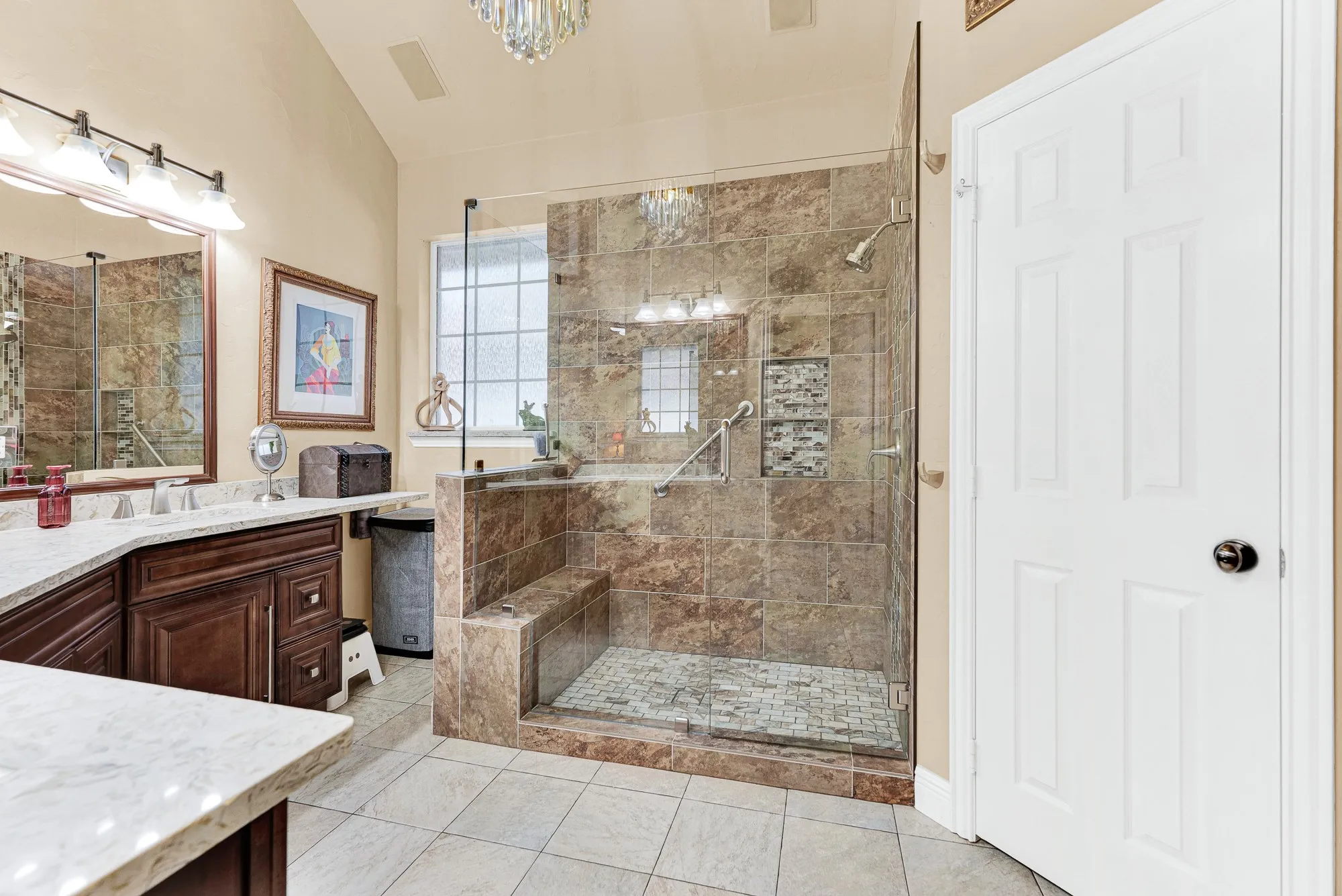 A frameless glass walk-in shower features full-height stone tile and a built-in bench, catch soft privacy-window sunlight. Picture starting your day with a long, refreshing steam session in your own spa-inspired hideaway