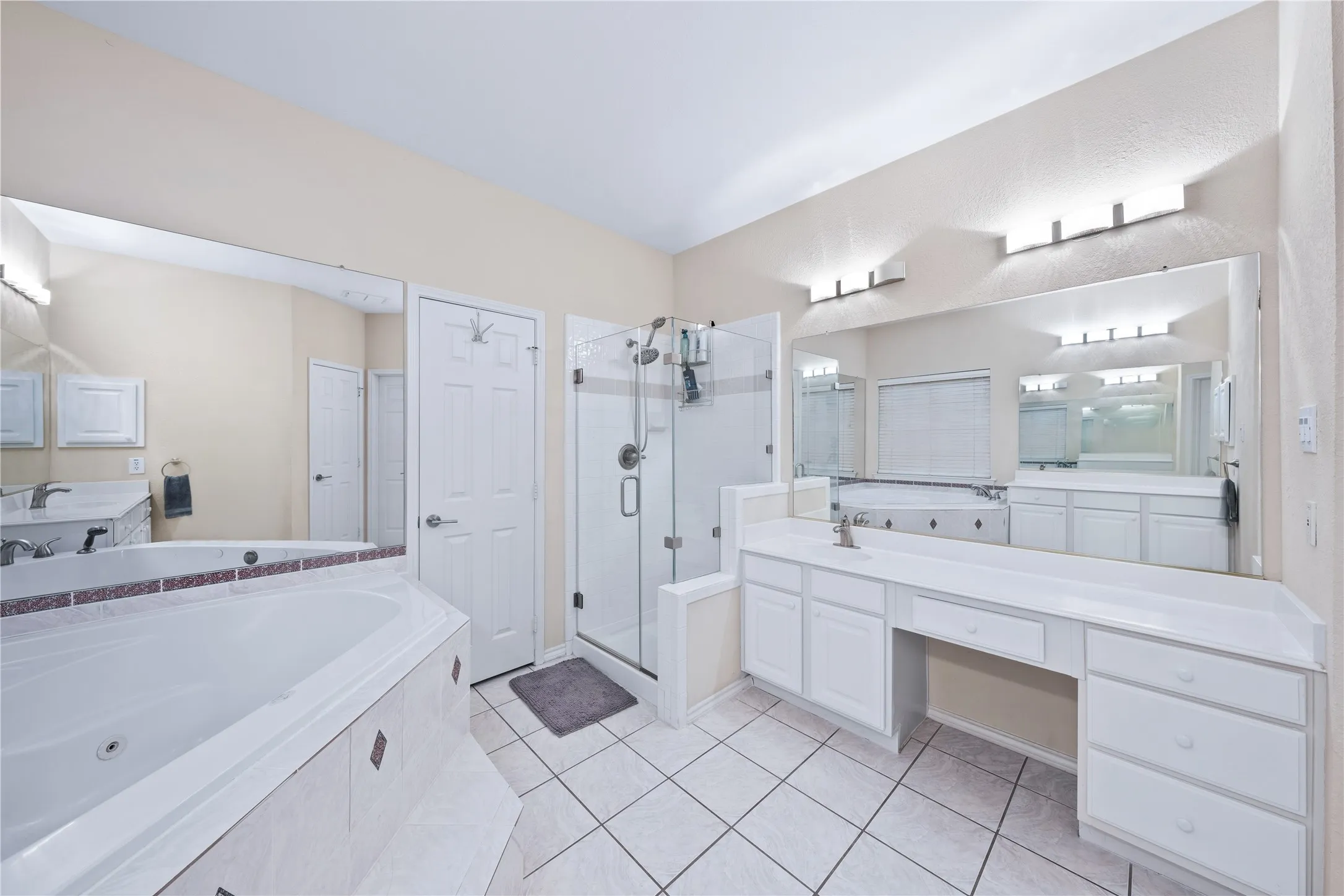 Walk-in shower with glass enclosure, separate soaking tub, expansive vanity with dual sinks, built-in vanity lighting, and tiled flooring