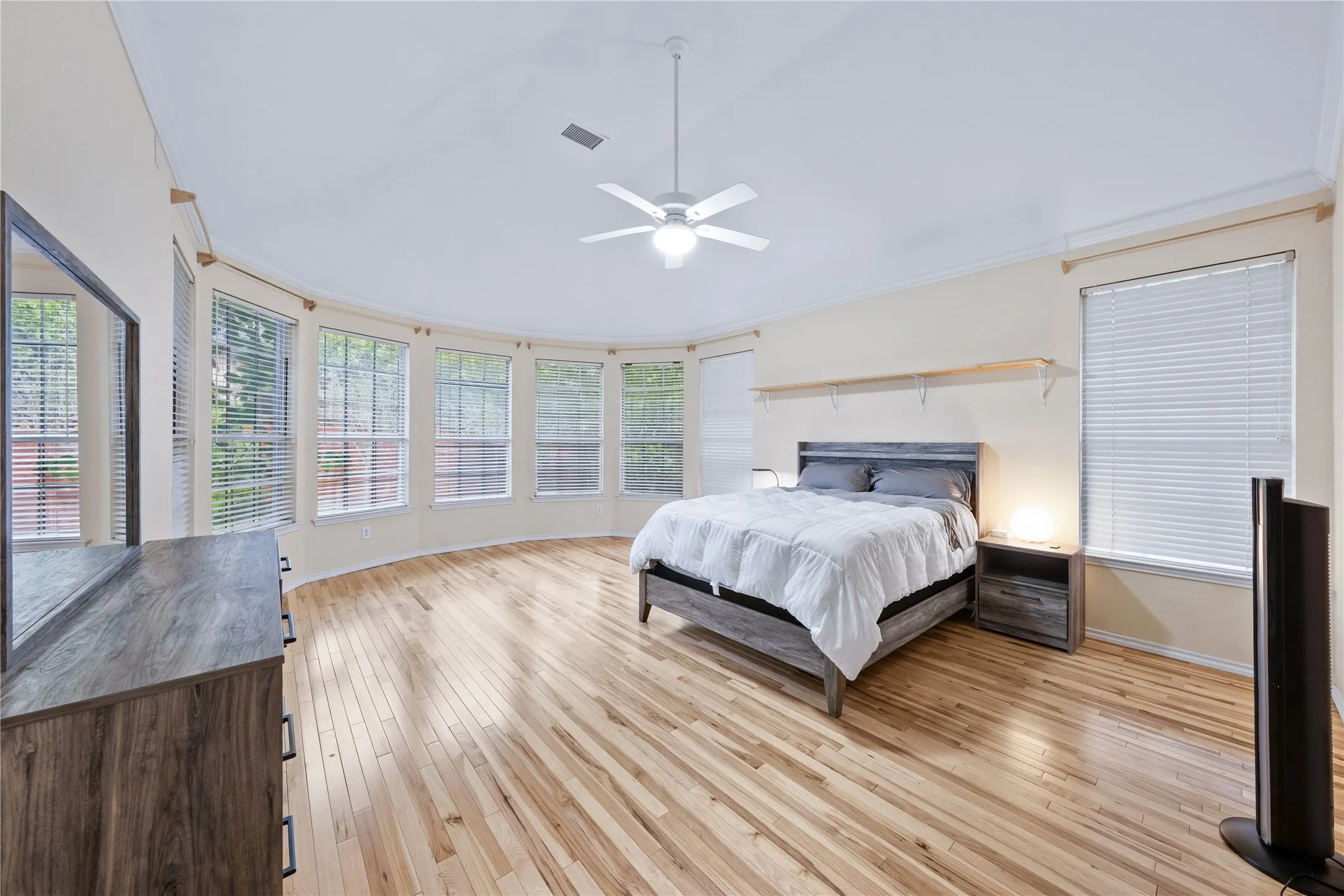 Hardwood flooring with a natural finish, ceiling fan, and multiple windows with blinds