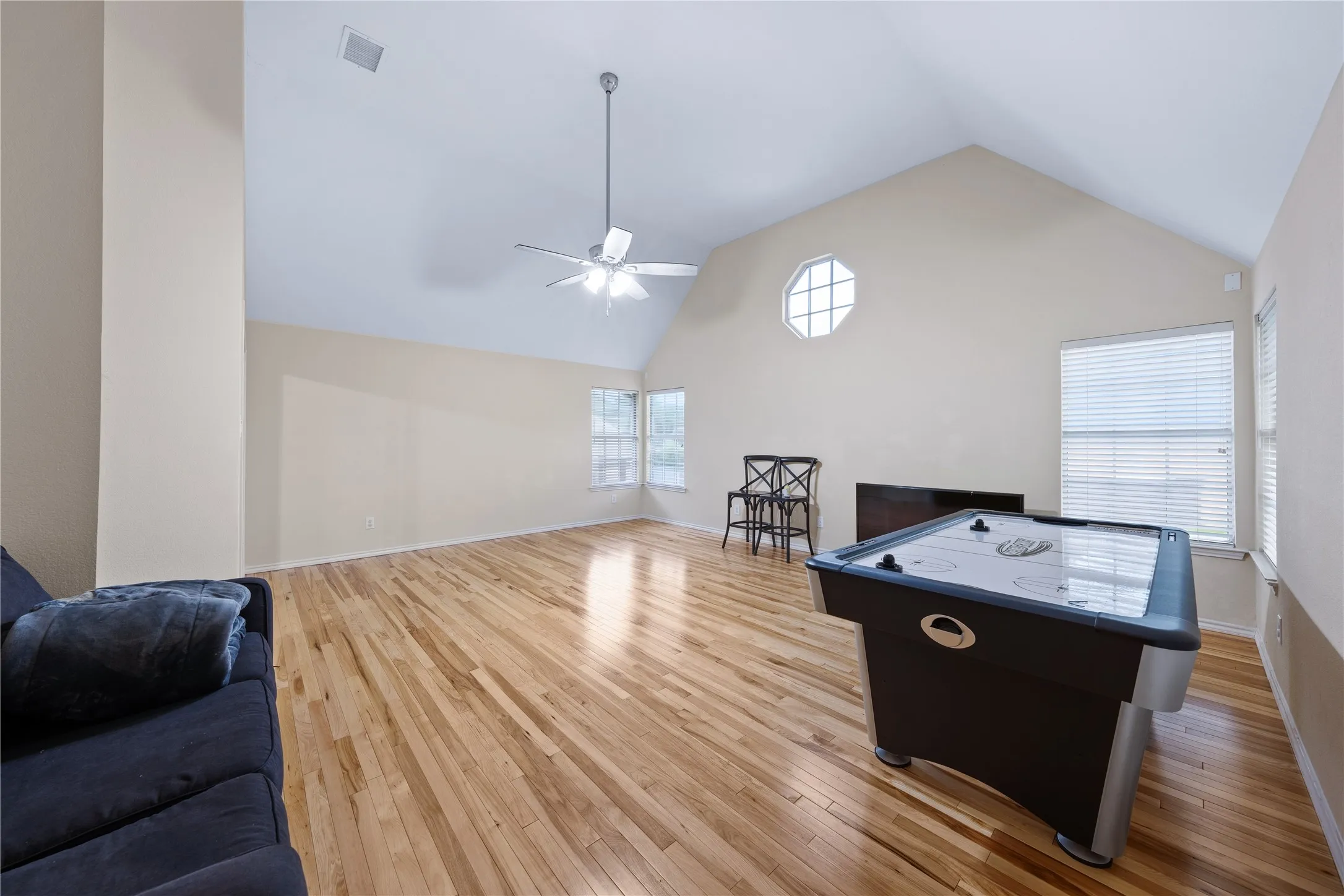Vaulted ceiling, ceiling fan, wood-finish flooring, octagonal window, and multiple windows with blinds