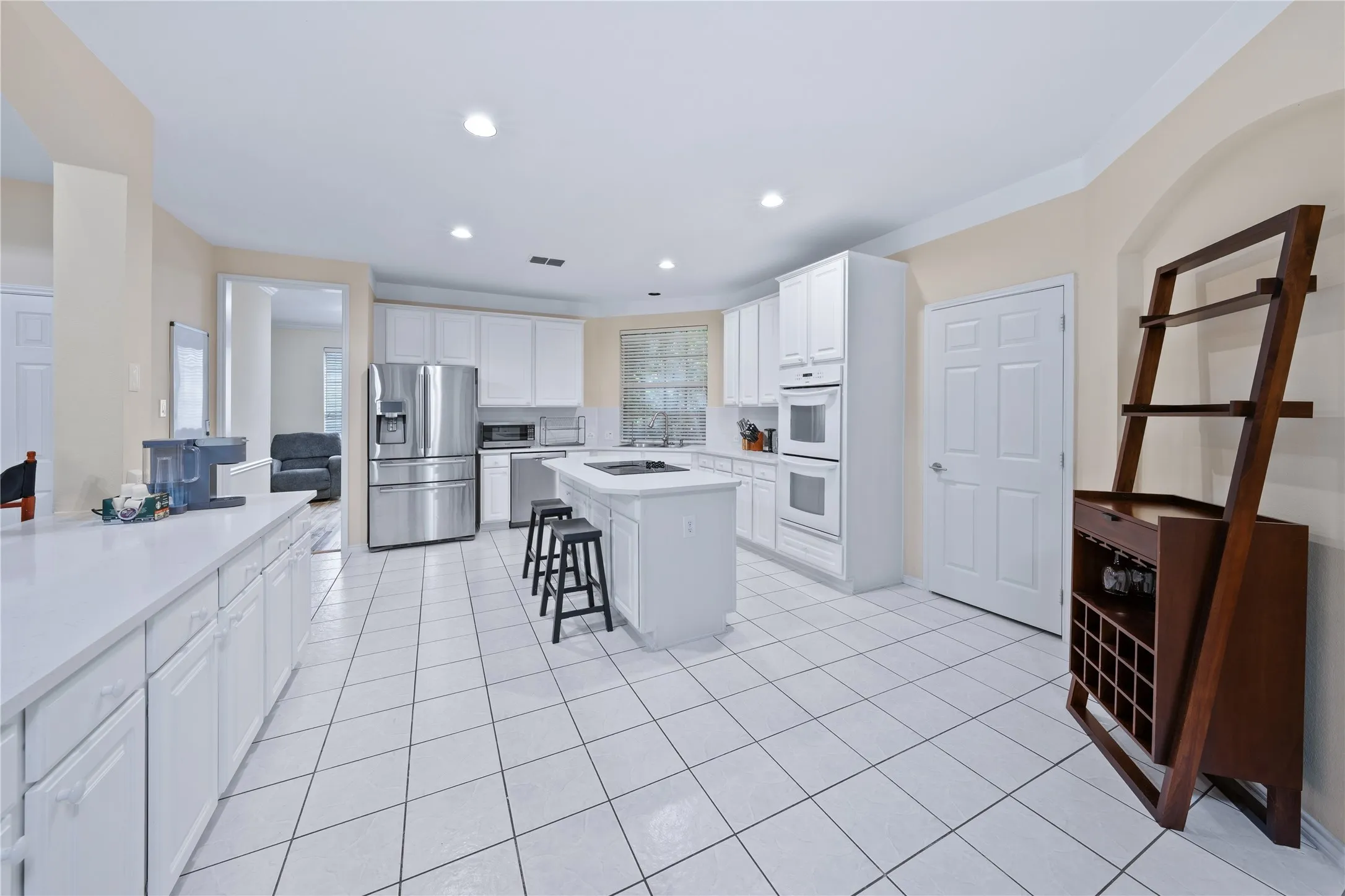 Kitchen featuring white cabinetry, white countertops, tile flooring, stainless steel appliances, and a central island with cooktop