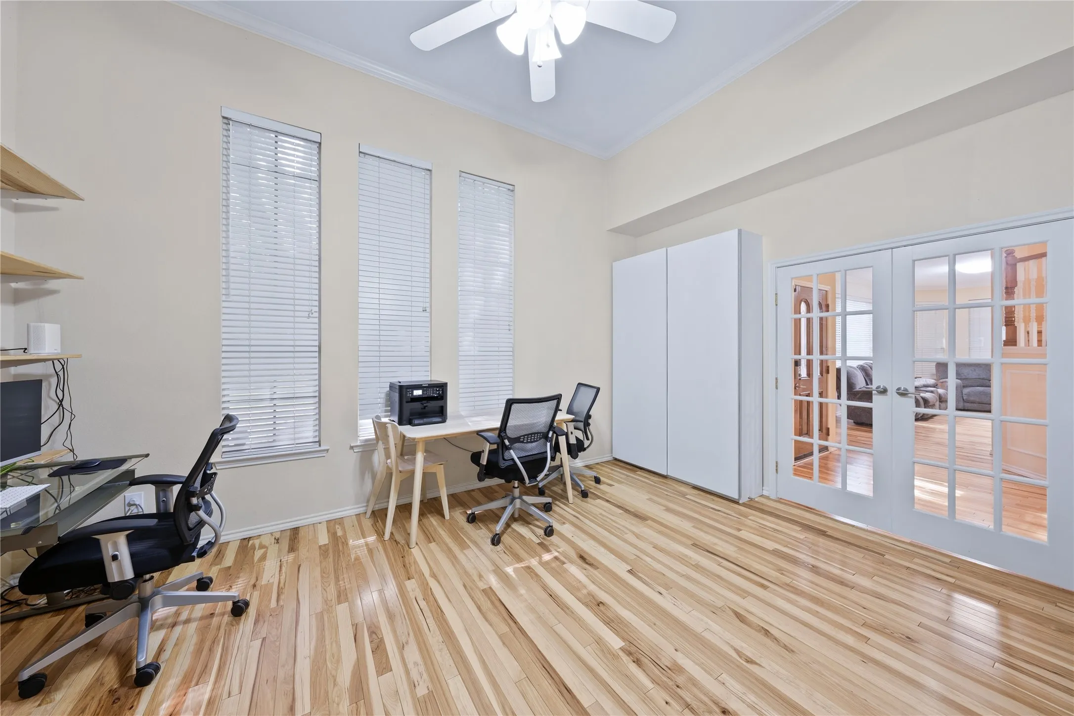 Tall ceilings with a ceiling fan, three vertical windows with blinds, wood-finish flooring, built-in storage cabinets, and French doors