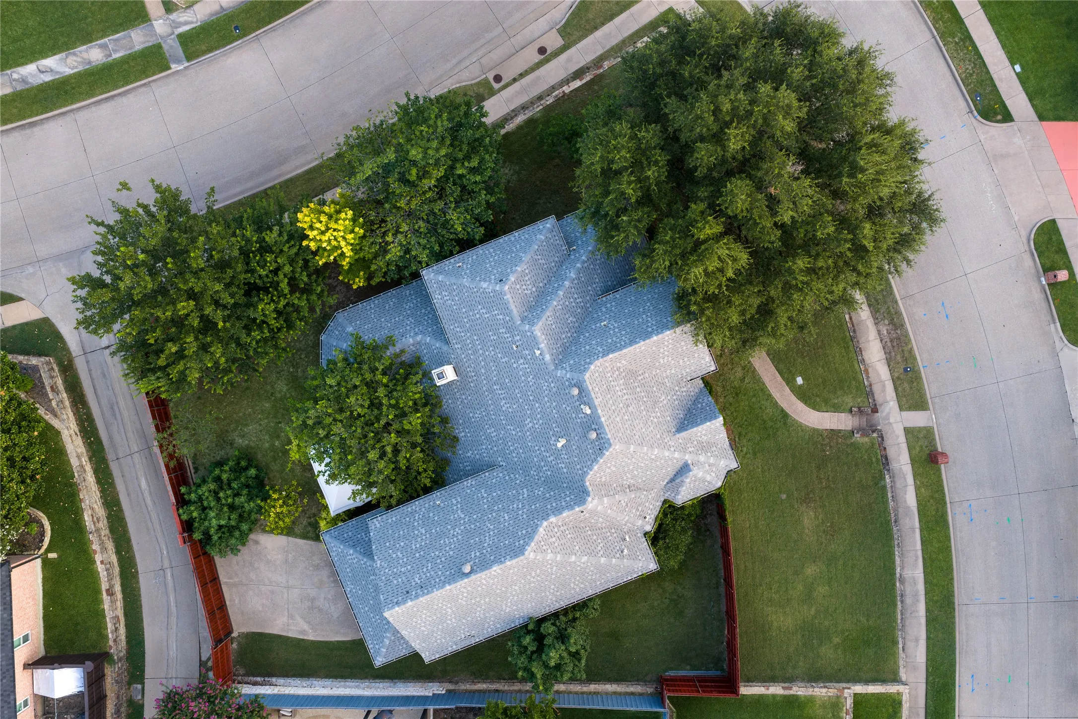 Gable-style roof with gray shingles, mature perimeter trees, concrete driveway, and established green lawn