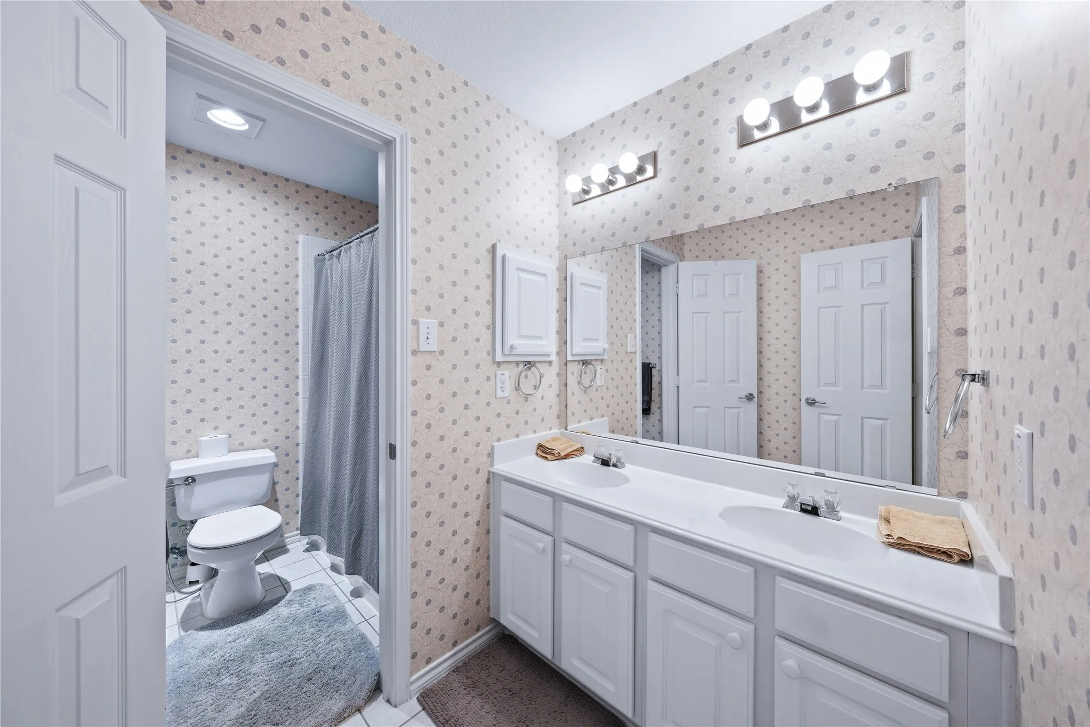 Dual vanity with integrated sinks, expansive wall-mounted mirror, brushed nickel light fixtures, white paneled cabinetry, and a built-in medicine cabinet