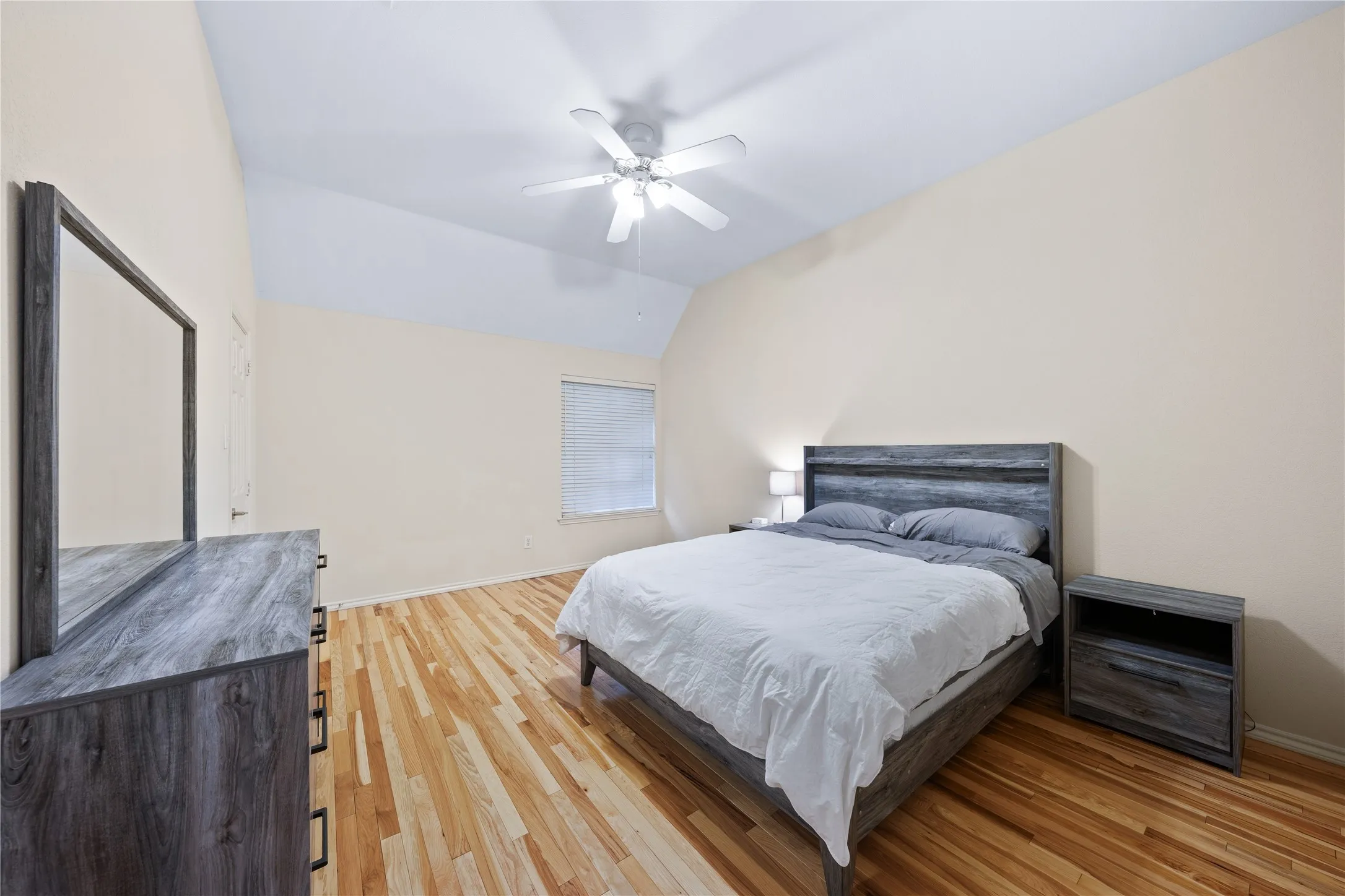 Vaulted ceiling with a ceiling fan, light wood-finish flooring, and a window with blinds