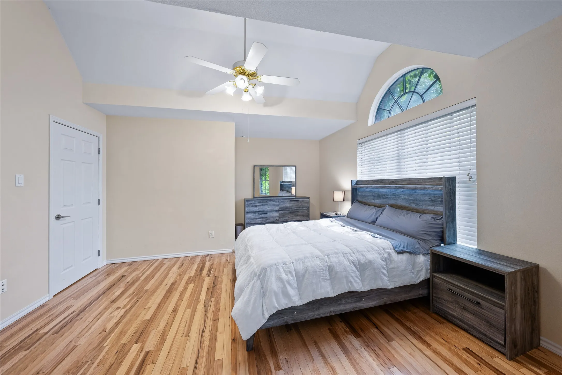 Vaulted ceiling, ceiling fan with integrated lighting, wood-finish flooring, half-round transom window, and window blinds