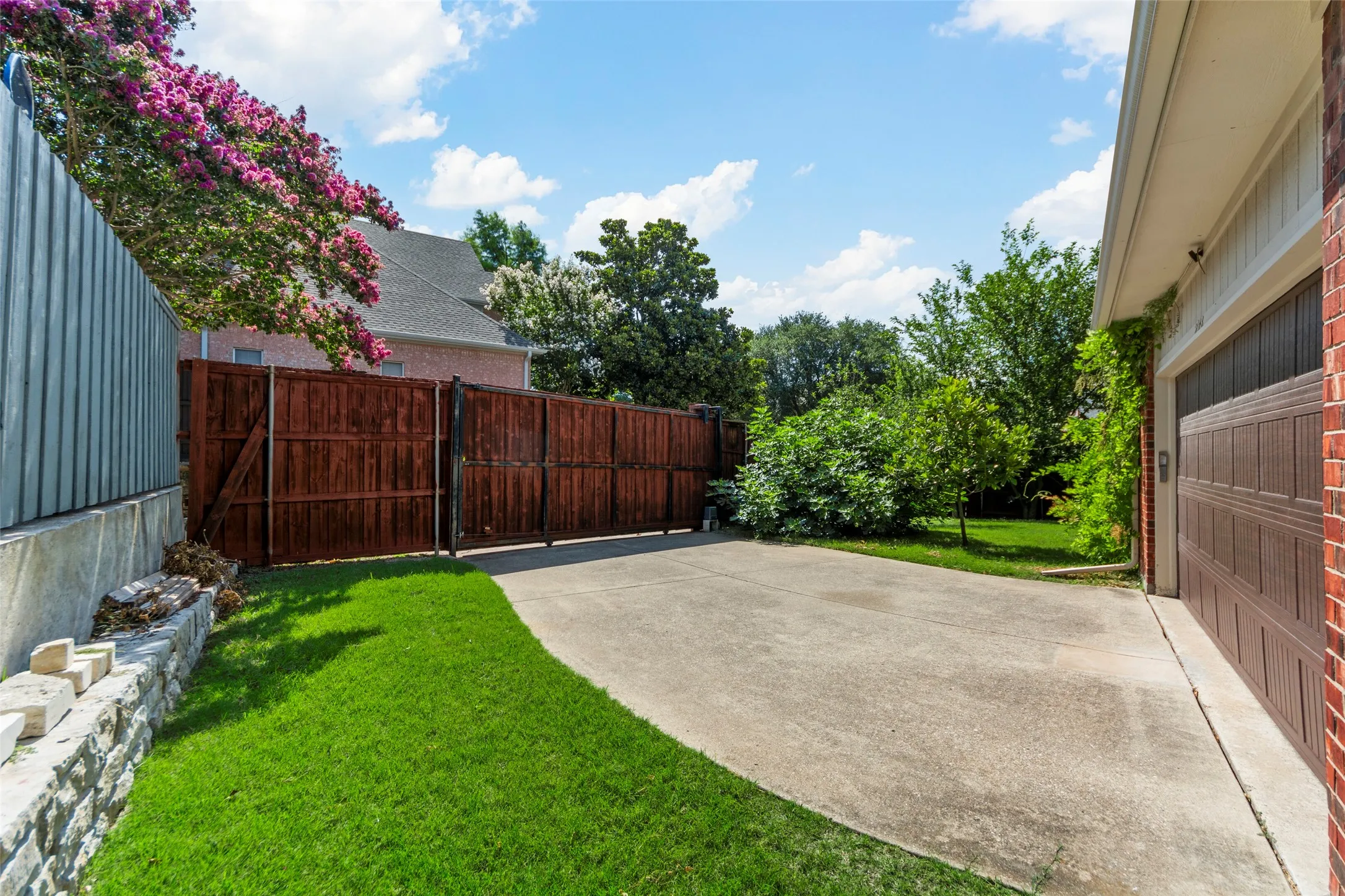 Expansive concrete driveway with a brown sectional garage door, brick facade, and a privacy fence