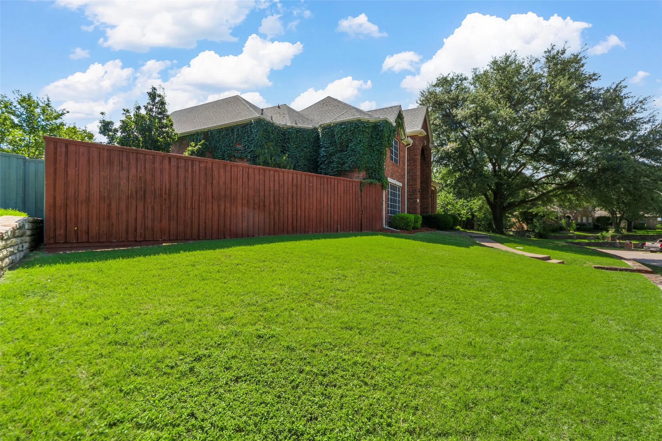 Expansive lawn with mature trees and a privacy fence, complemented by brick exterior detailing and an ivy-covered facade