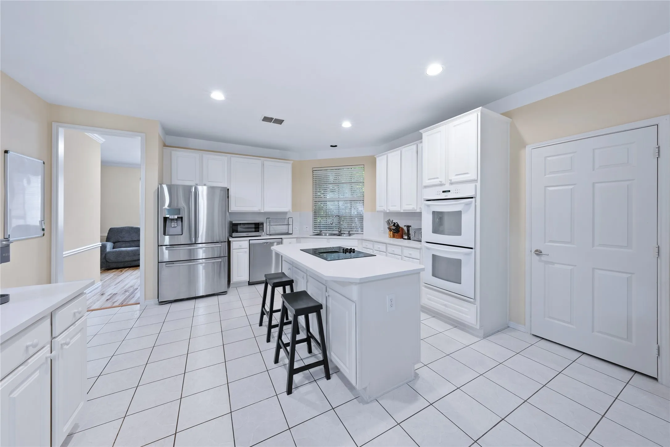 Kitchen featuring white cabinetry, white countertops, built-in double ovens, stainless steel refrigerator, and tiled flooring