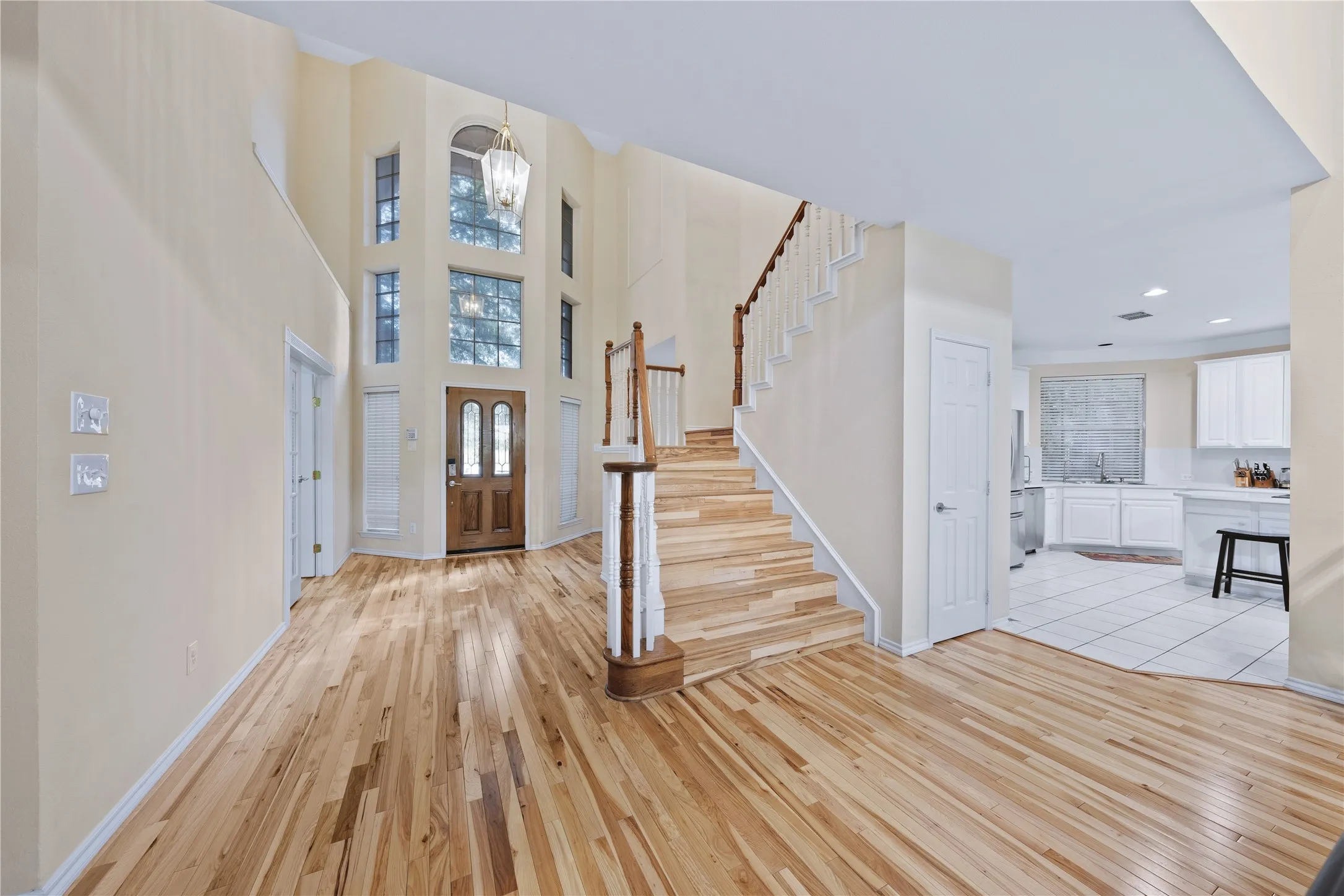 Two-story foyer with natural wood-finish flooring, a grand staircase with wood newel posts, and a decorative chandelier