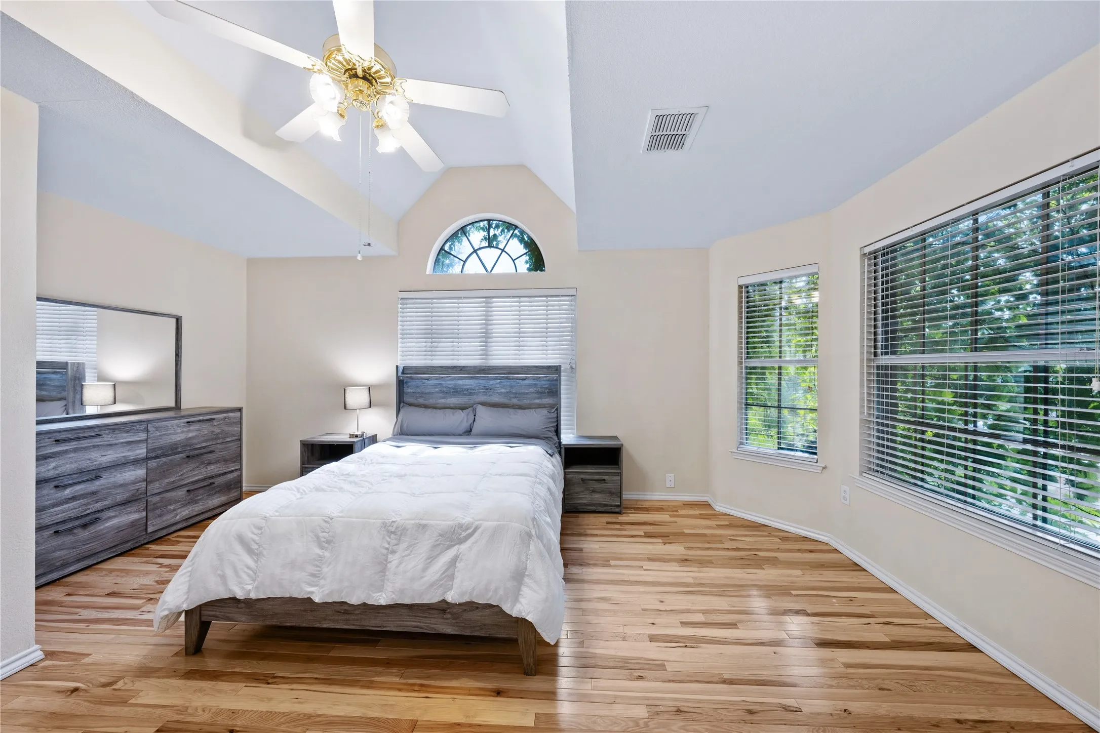 Vaulted ceiling, hardwood flooring, arched window, ceiling fan, and multiple windows