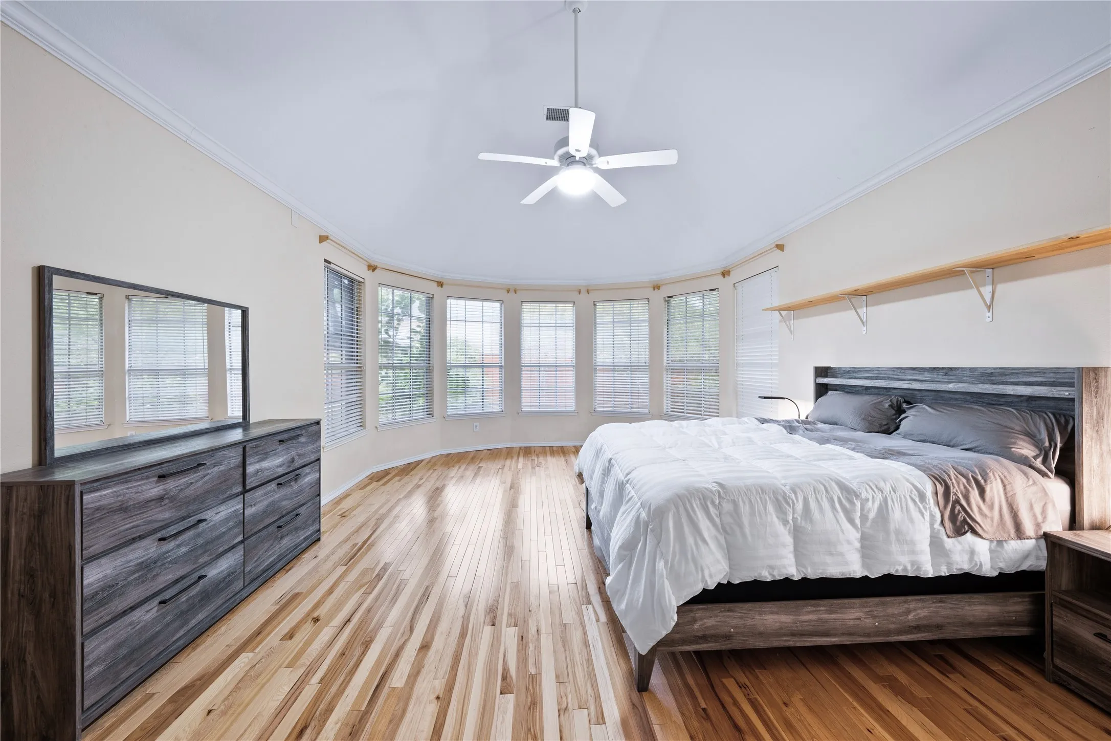 Hardwood flooring, curved bay window, crown molding, ceiling fan, and built-in shelving