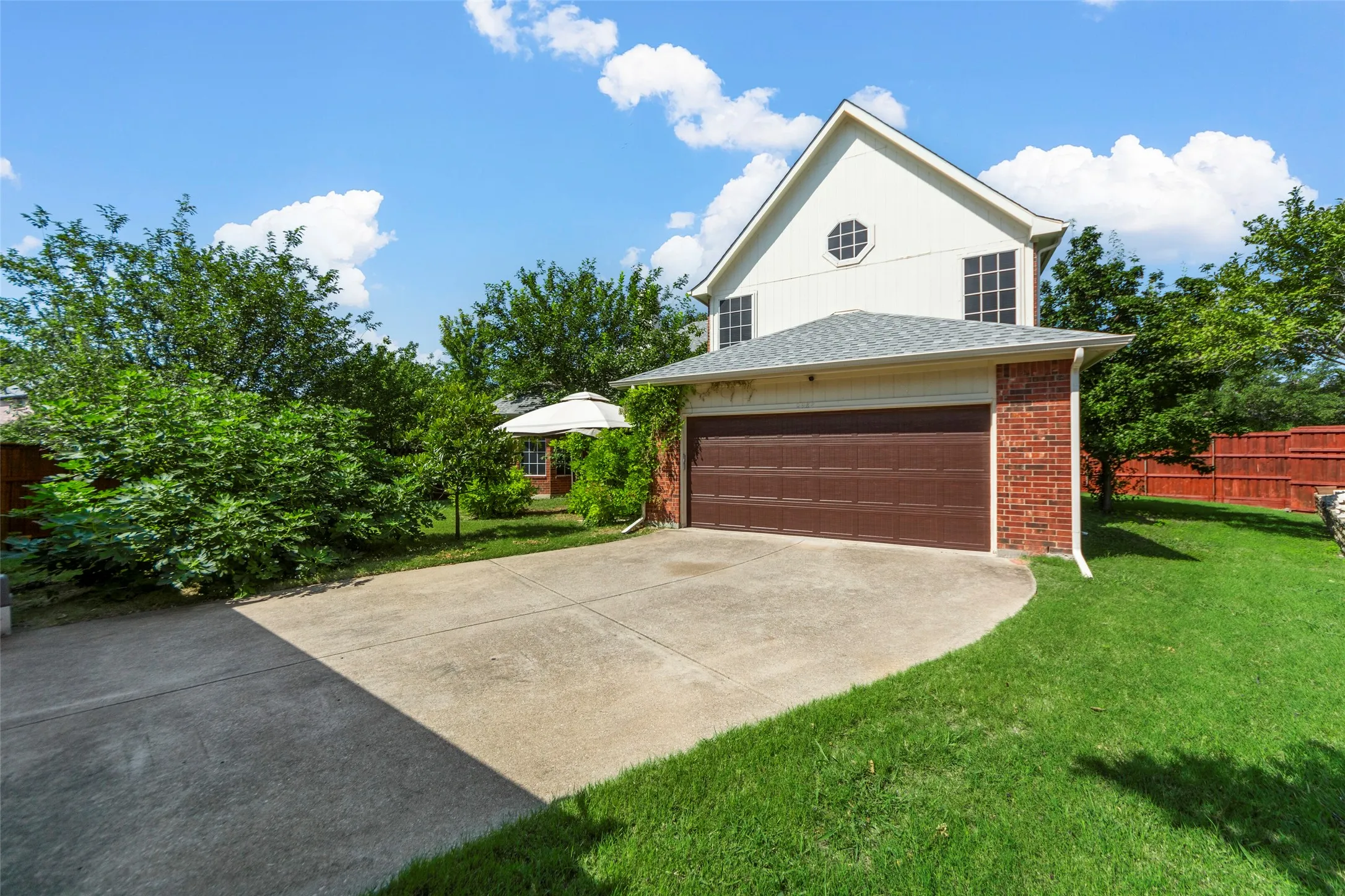 Two-story exterior with brick and siding, a two-car garage, mature landscaping, and a fenced backyard