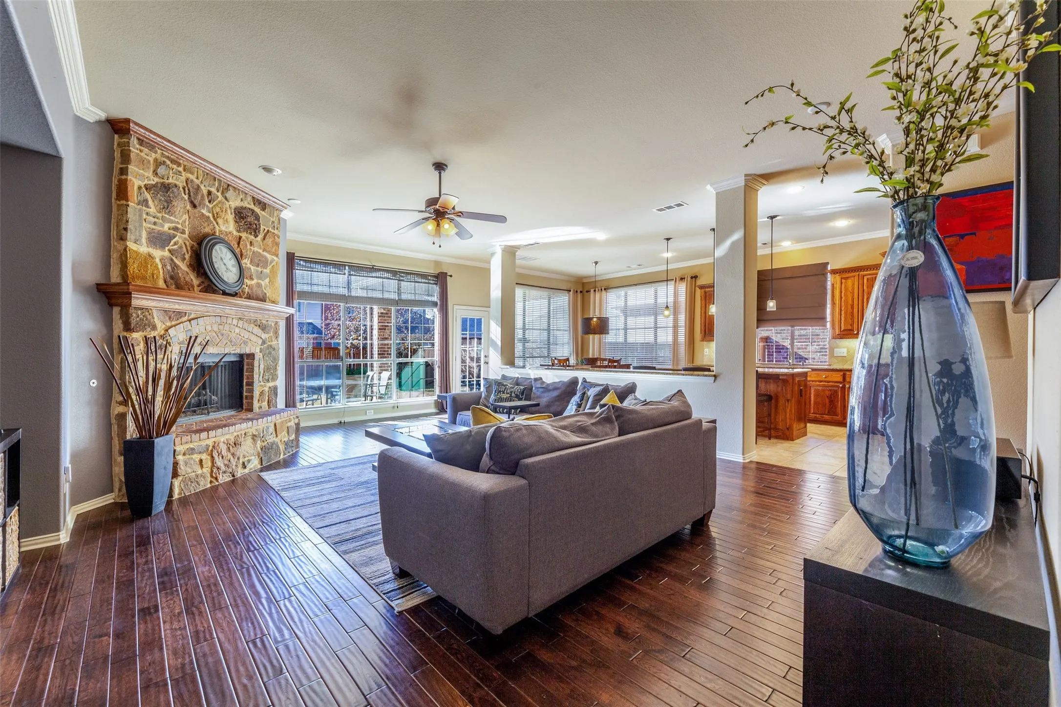 Living room with a stone fireplace, hardwood / wood-style floors, ceiling fan, and crown molding