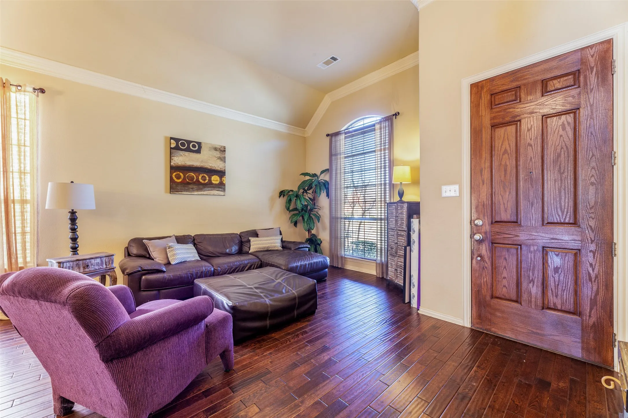 Living room with vaulted ceiling, crown molding, hardwood / wood-style flooring, and visible vents