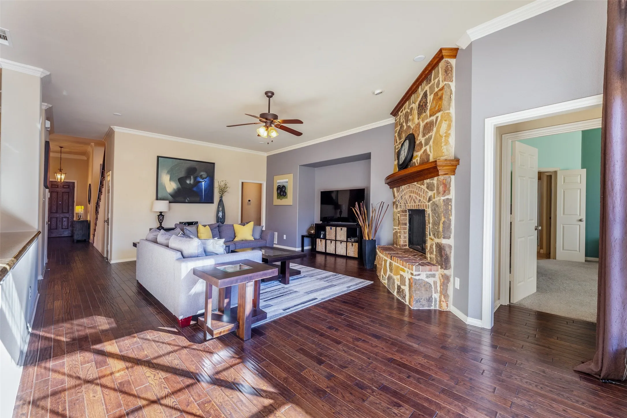 Living area with ornamental molding, a fireplace, a ceiling fan, and wood-type flooring