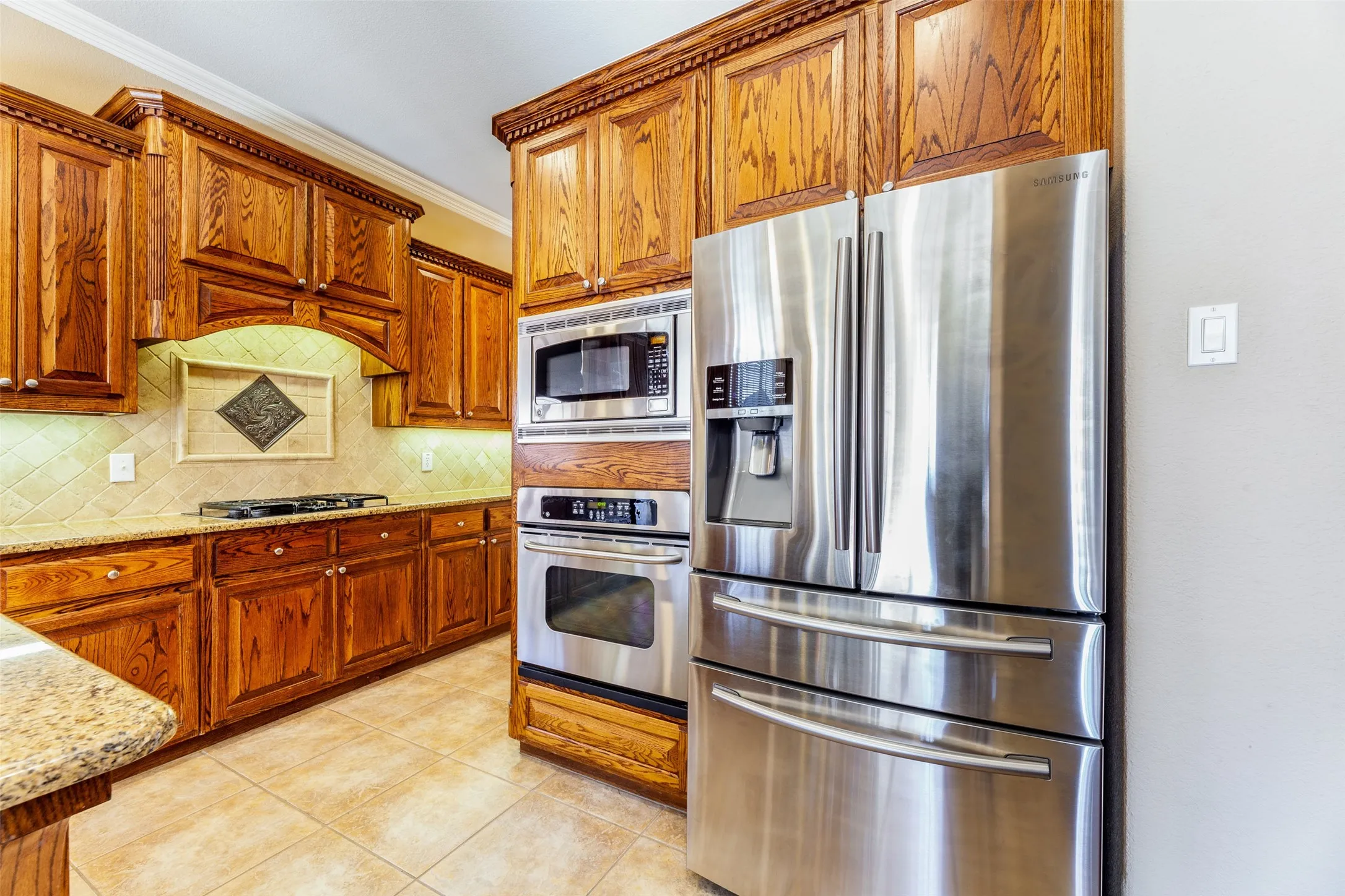 Kitchen featuring stainless steel appliances, light tile patterned flooring, light stone counters, crown molding, and backsplash