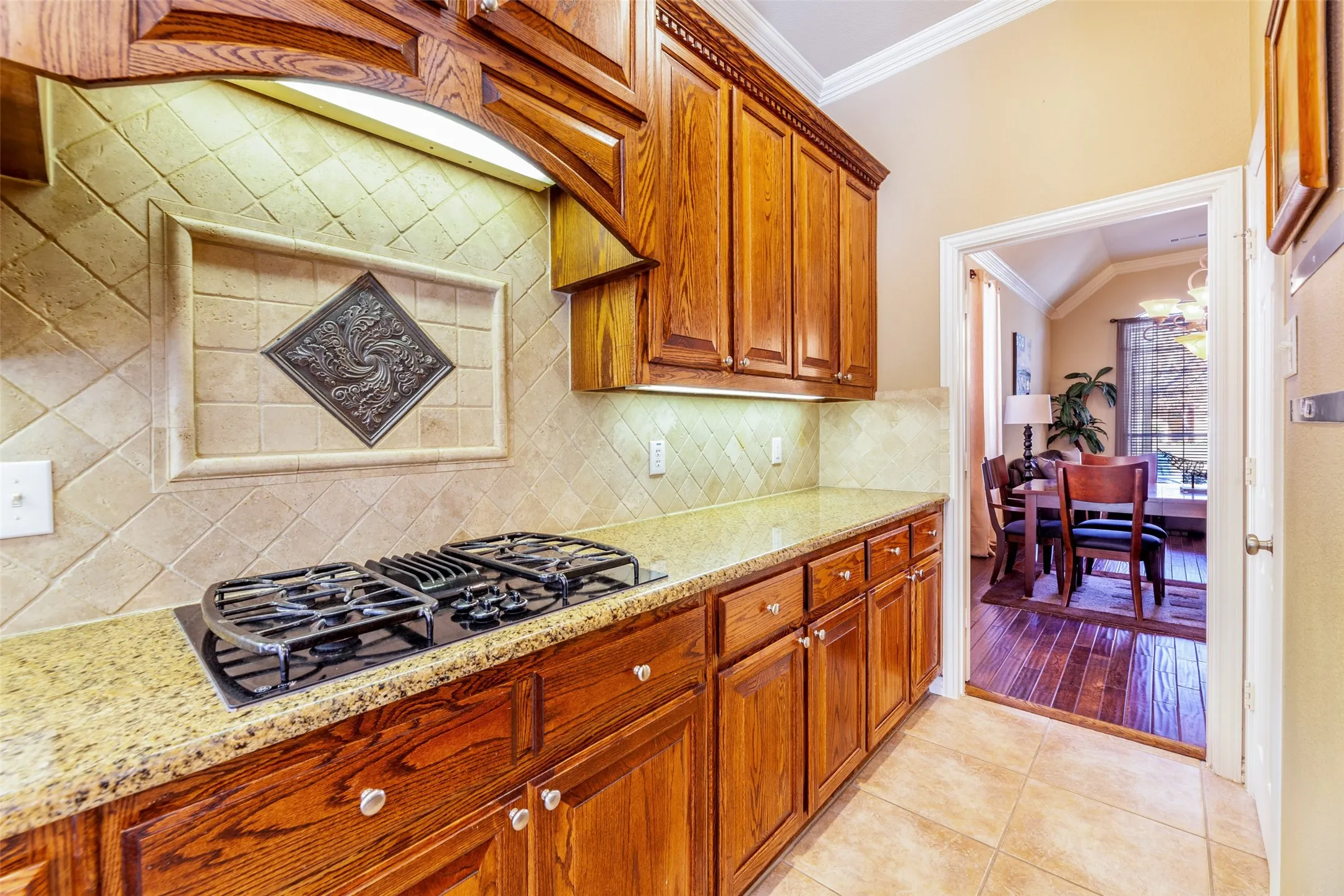 Kitchen with light tile patterned floors, brown cabinetry, black gas stovetop, crown molding, and light stone countertops