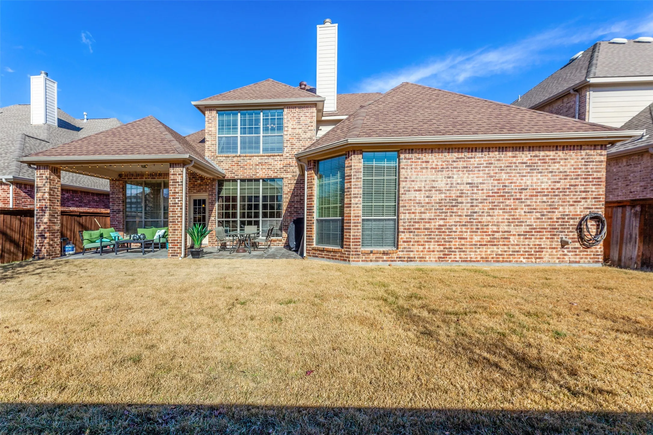 Rear view of property featuring roof with shingles, a patio, brick siding, and a lawn