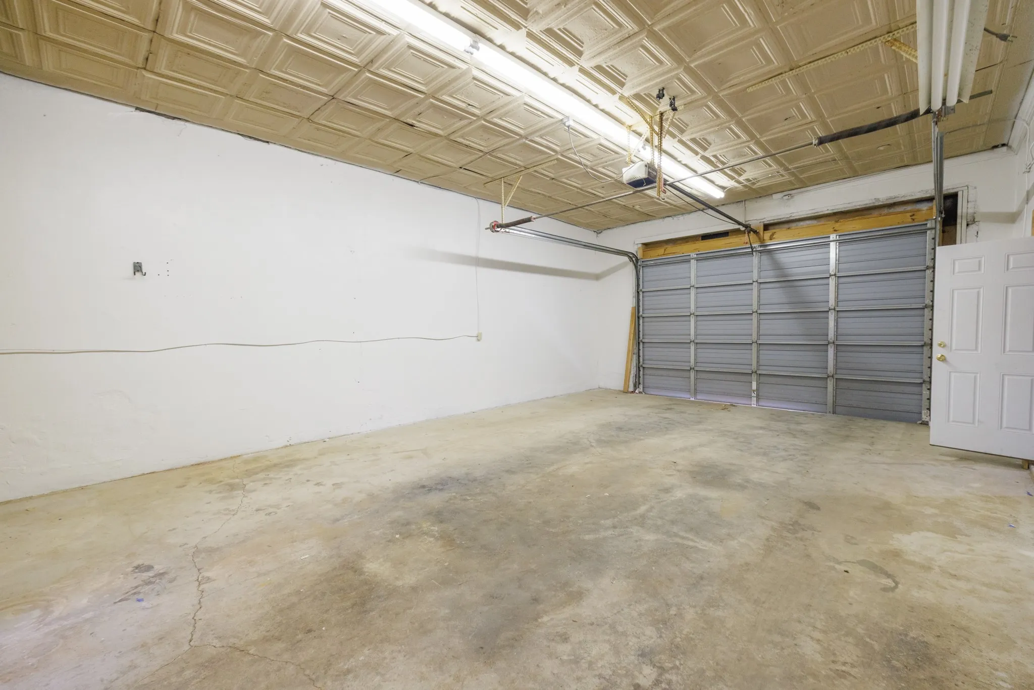 Attached garage featuring a corrugated metal roll-up door, an interior access door, a concrete floor, and a textured ceiling