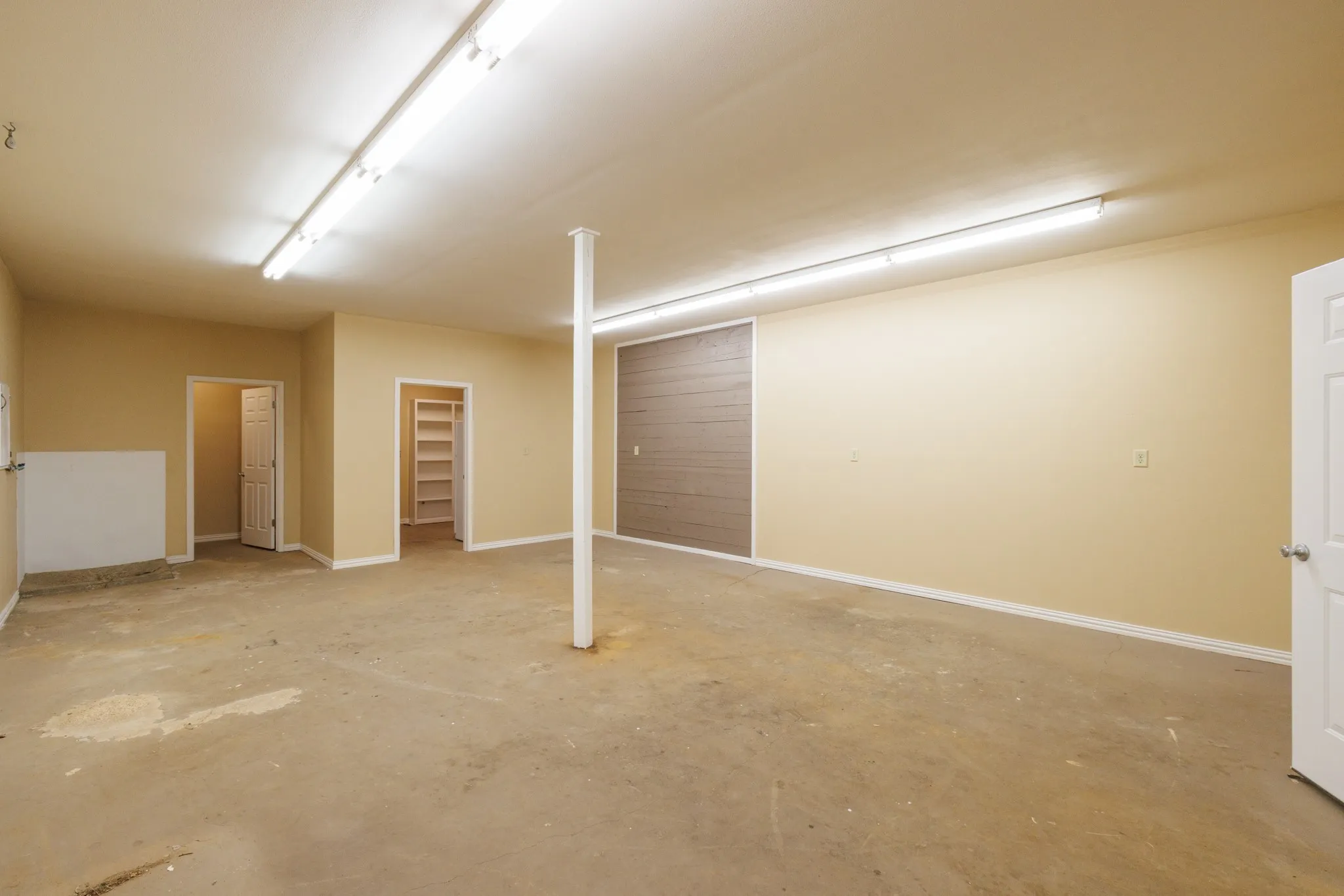Spacious interior with neutral wall tones, concrete flooring, overhead fluorescent lighting, and built-in shelving