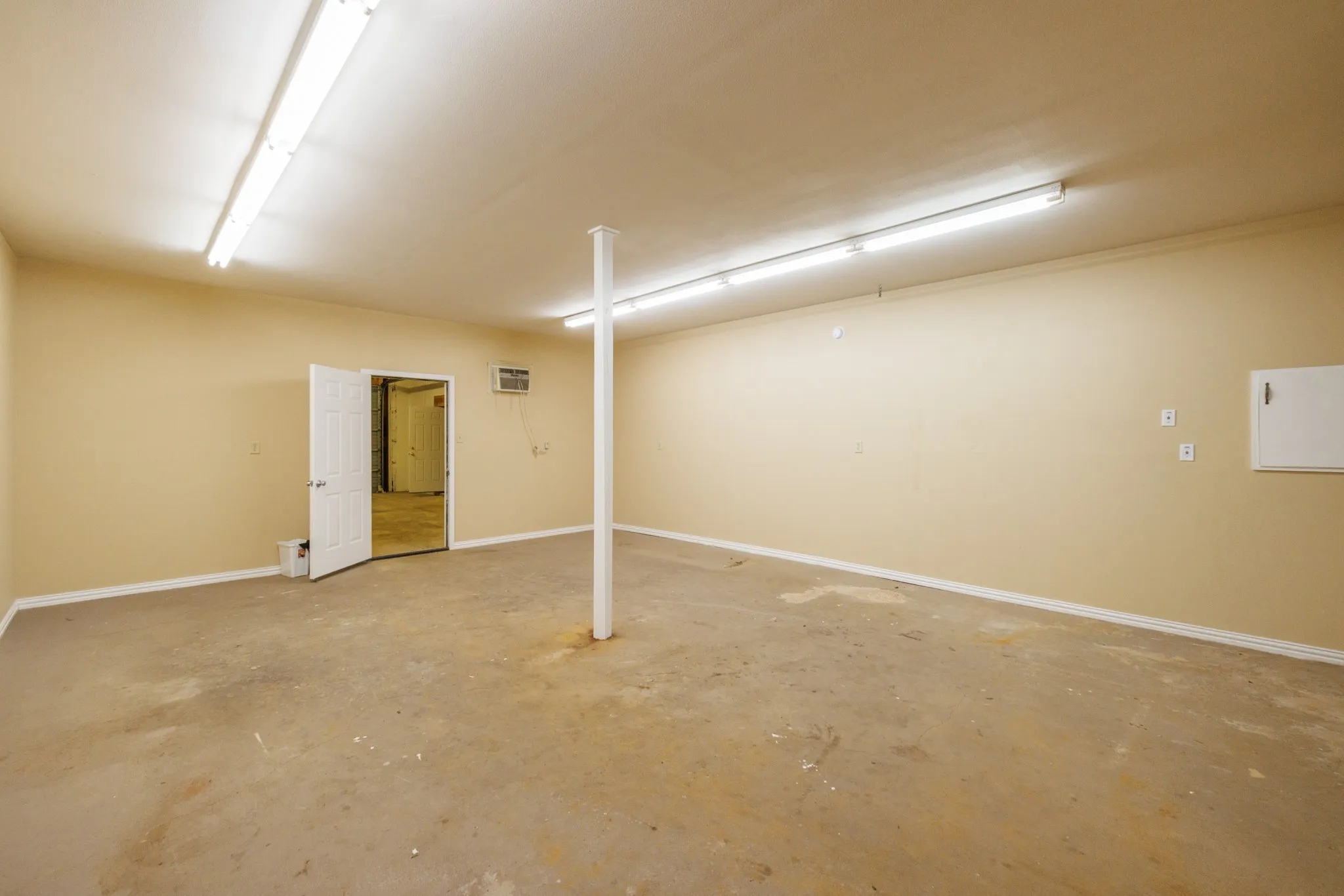 Spacious room with concrete flooring, cream-colored walls, and fluorescent ceiling lights