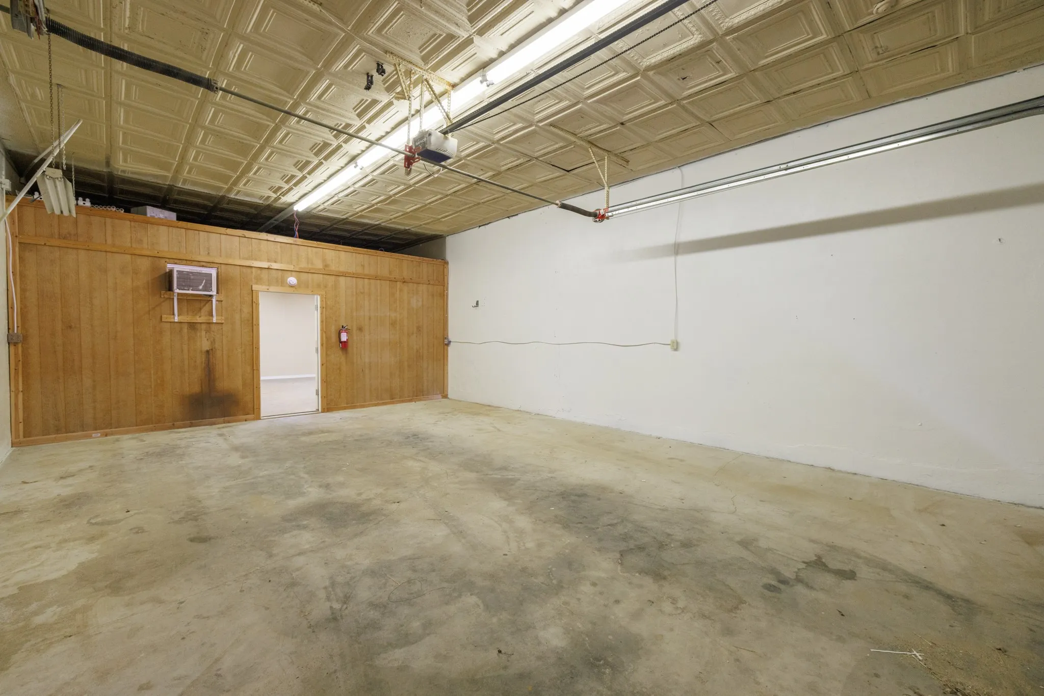 Concrete flooring, wood-paneled wall, white painted wall, exposed ceiling system, fluorescent lighting fixtures