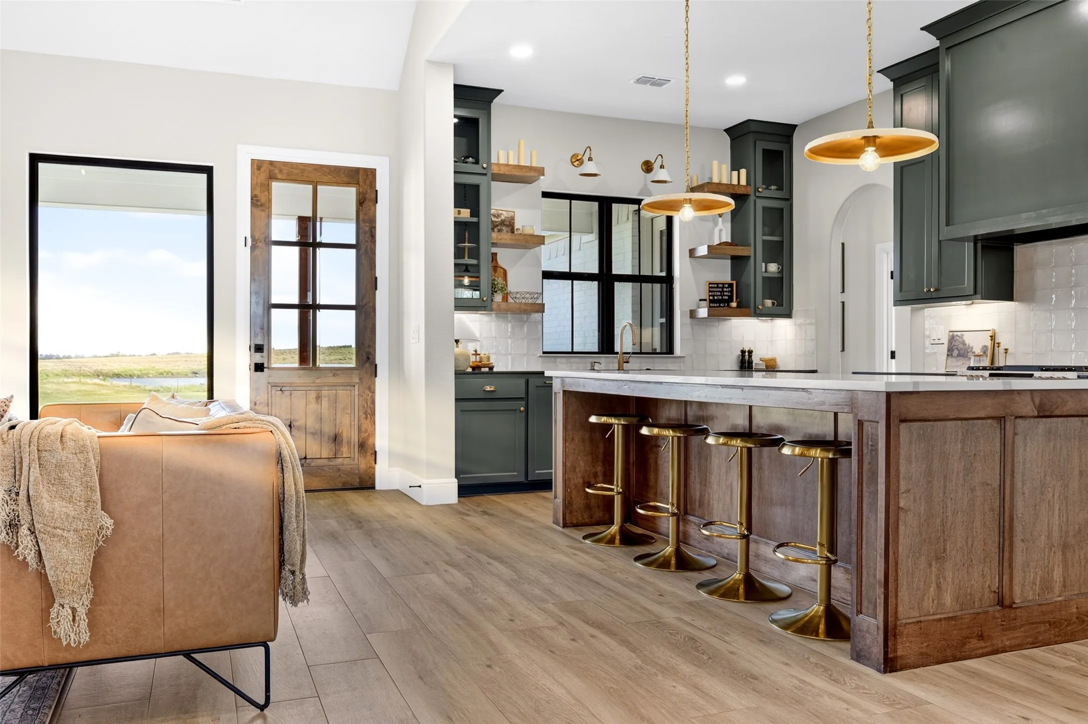 Wood-finish flooring, dark green cabinetry, a central kitchen island with a light-toned countertop, and a glass-paneled wooden door