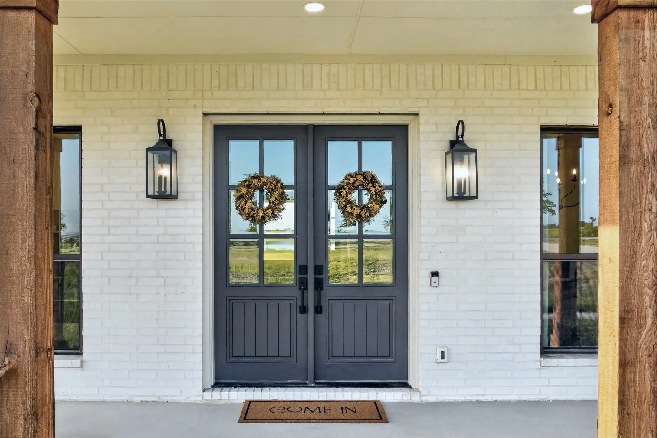 Welcoming entry featuring dual dark-finish French doors with glass panes and vertical plank detailing, flanked by symmetrical black lantern sconces