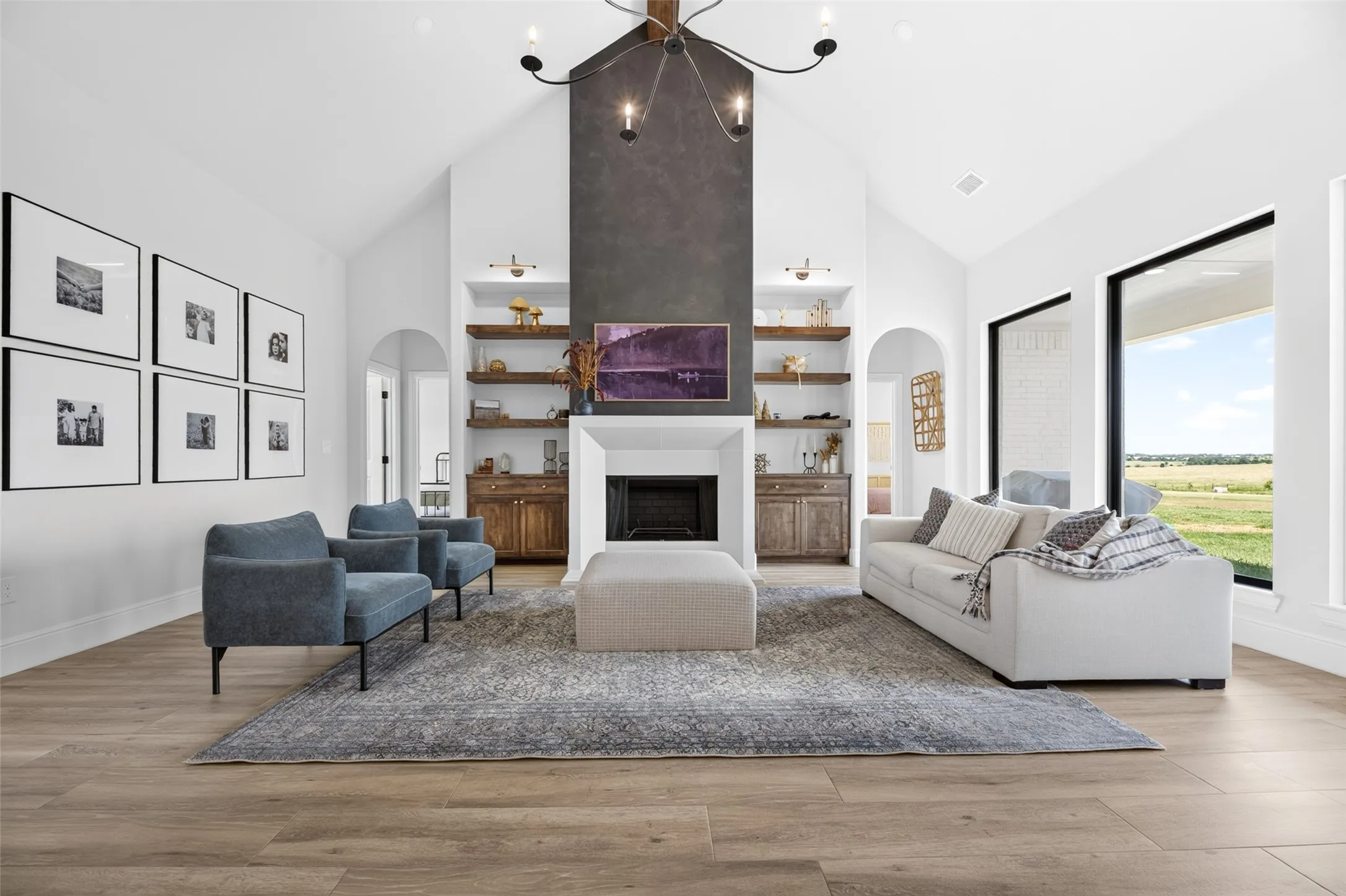 Vaulted ceiling, wood-finish flooring, recessed fireplace with dark surround, built-in shelving, and expansive windows