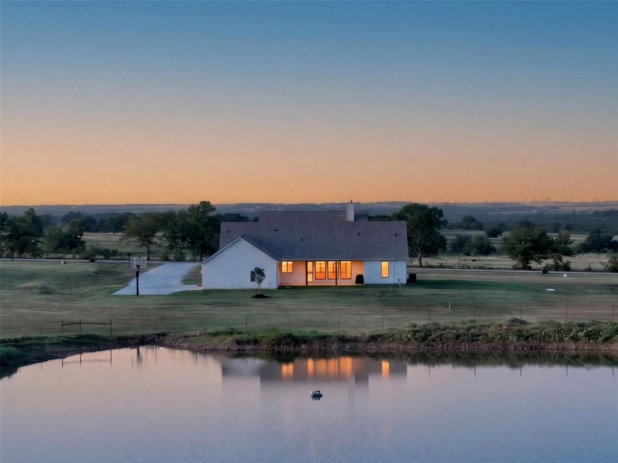Expansive backyard featuring a private pond, concrete driveway, and a white exterior home with a dark roof