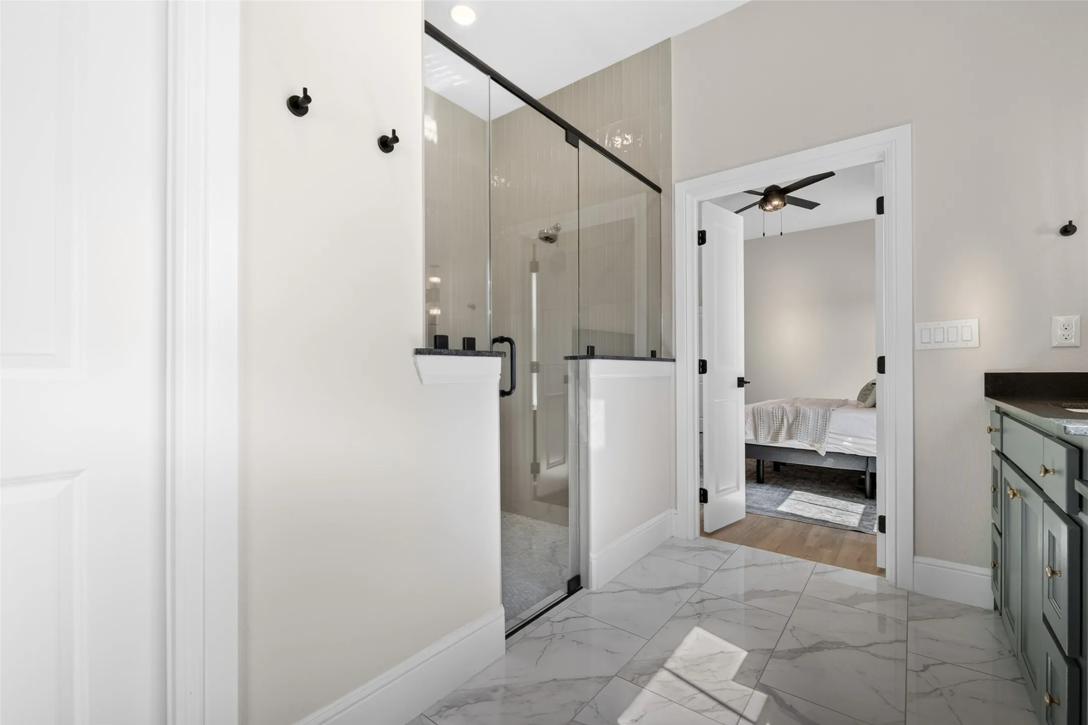 Glass-enclosed shower with matte black hardware, tiled shower surround, marble-finish floor tiles, and a built-in vanity with dark countertop