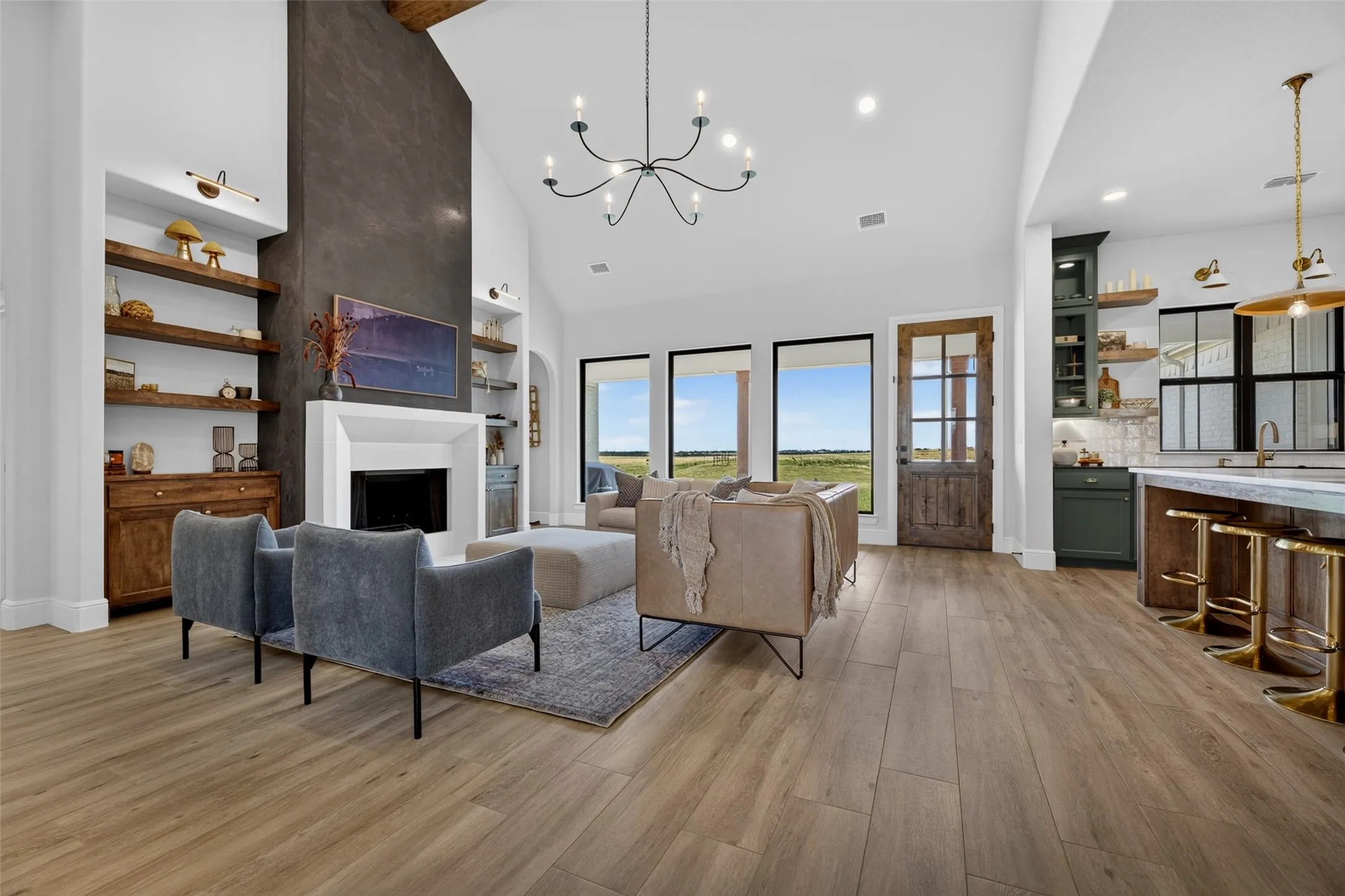 Open-concept living space featuring soaring ceilings with exposed wood beams, a modern chandelier, and abundant natural light from expansive multi-pane windows