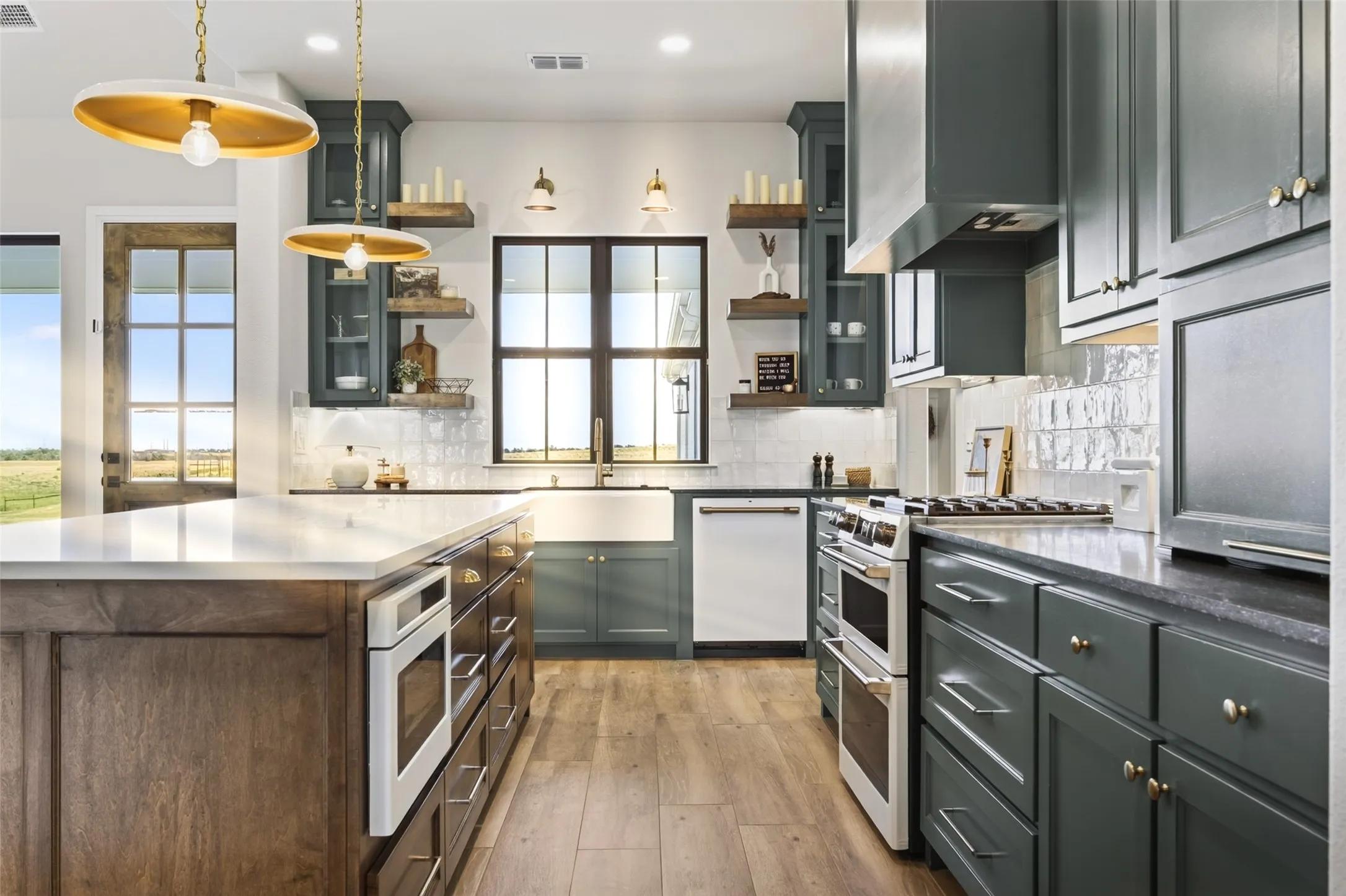 Gourmet kitchen featuring a large central island with integrated oven, custom cabinetry, wood-finish flooring, a farmhouse sink, and contemporary pendant lighting