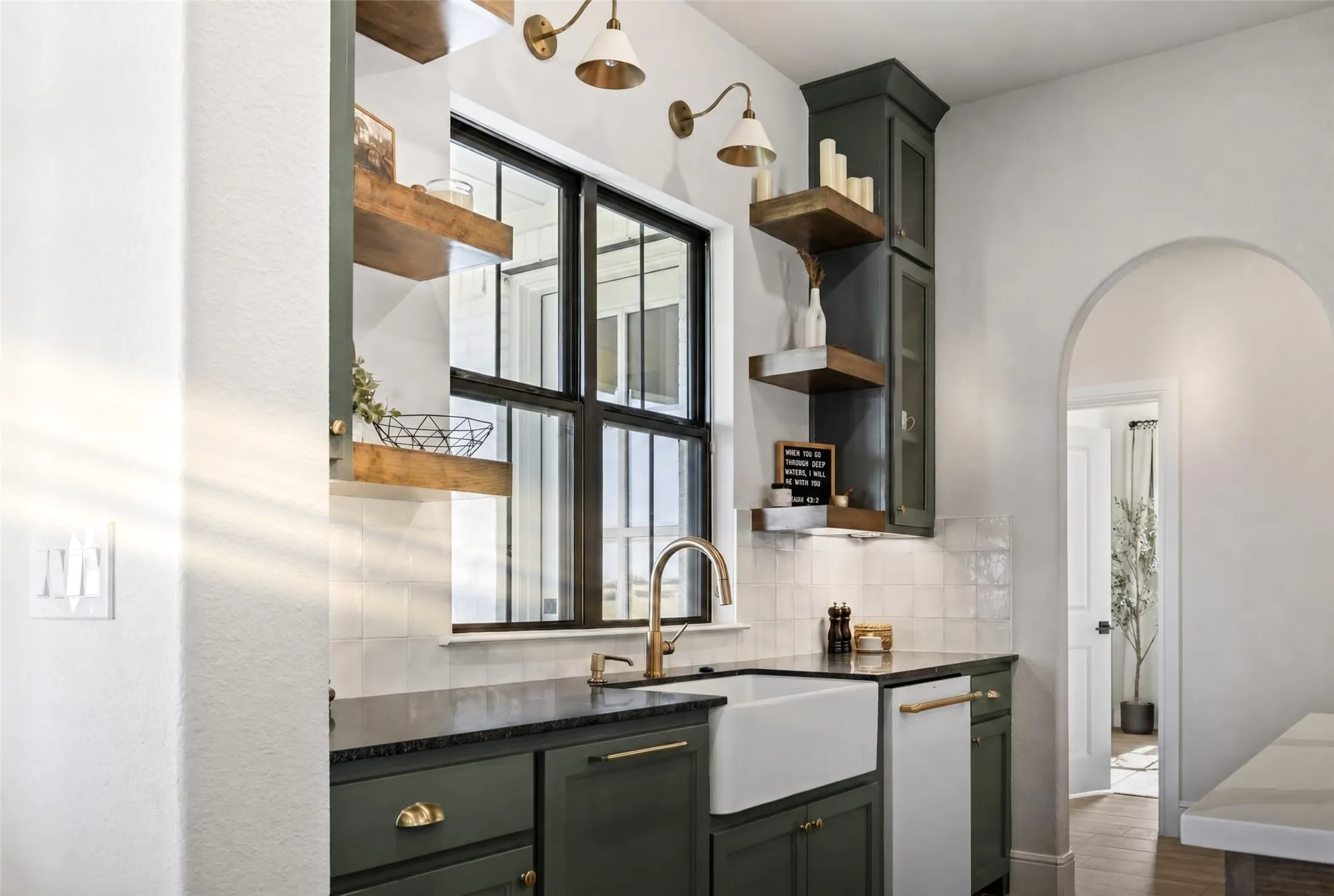 Elegant wet bar featuring a farmhouse-style sink with brass gooseneck faucet, dark cabinetry with brass hardware, white subway tile backsplash, and a dark countertop