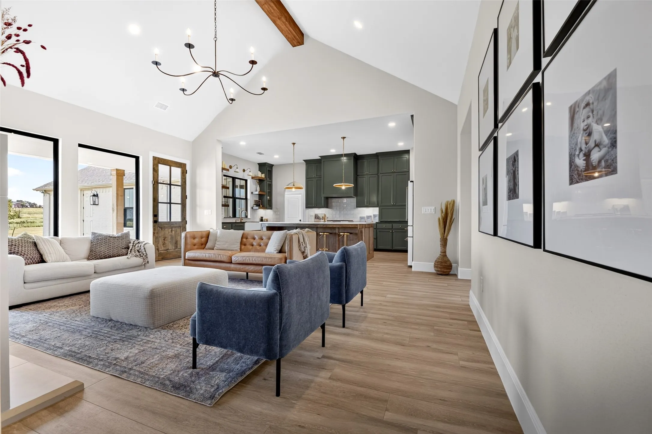 Vaulted ceiling with exposed wood beam, open-concept design, wide-plank wood-finish flooring, recessed lighting, and a modern chandelier