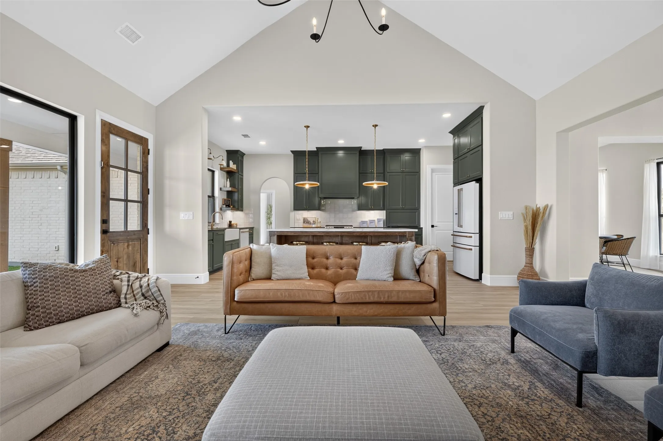 Vaulted ceiling, wood-finish flooring, custom wood and glass door, arched entryway, and dark-toned kitchen cabinetry