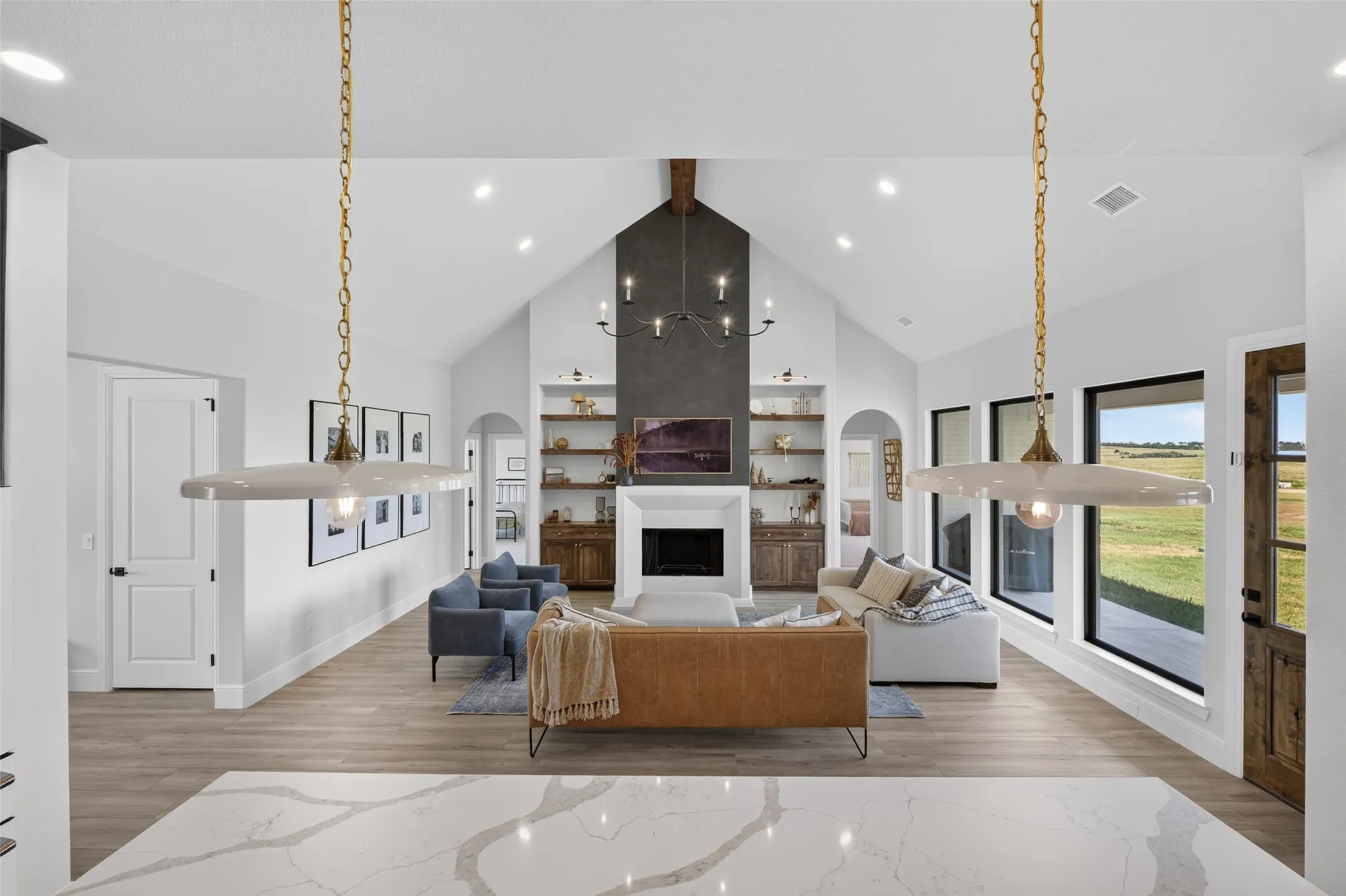 Vaulted ceiling with recessed lighting, floor-to-ceiling fireplace with mantel and built-in shelving, wood-finish flooring, and a large window with exterior access