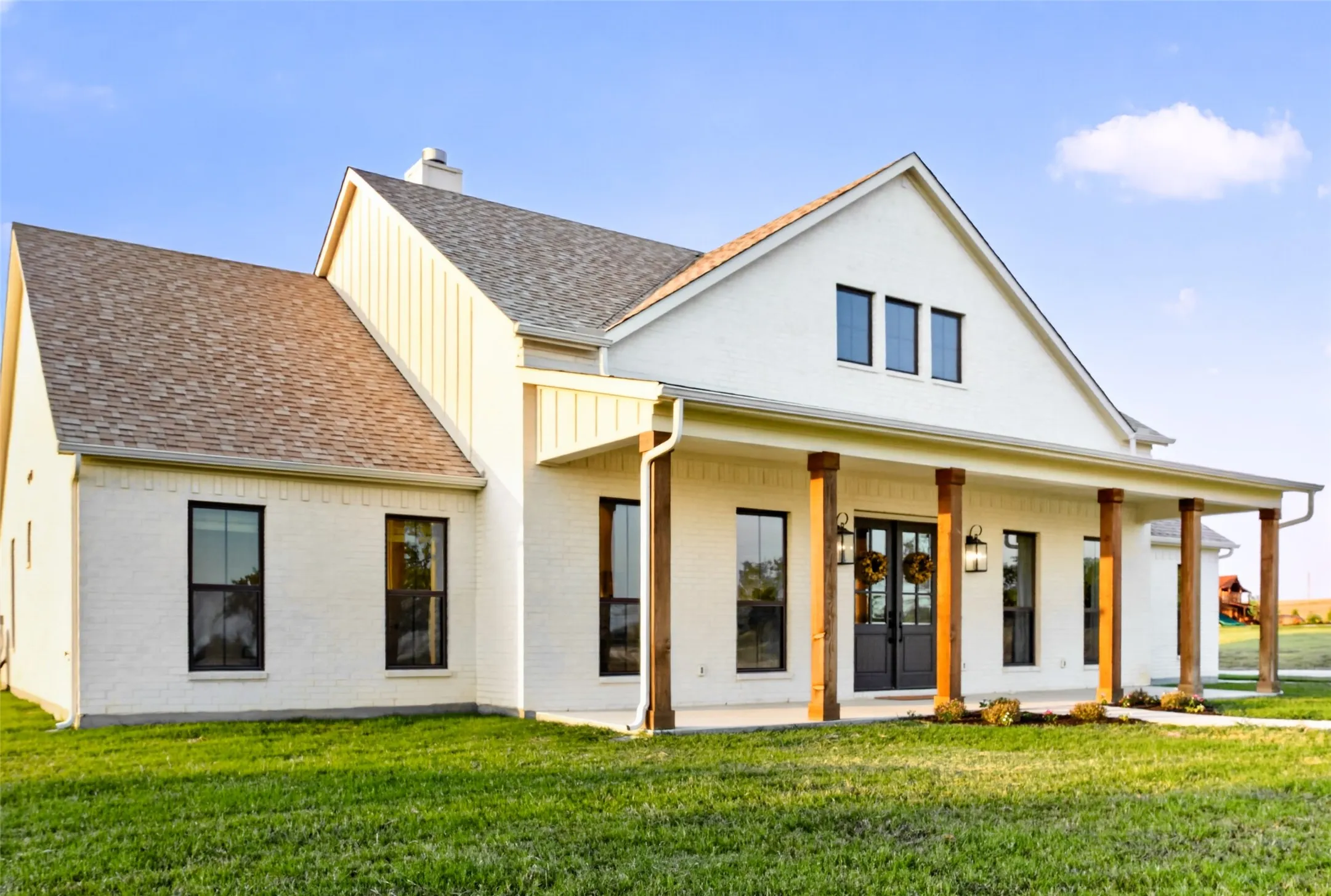 Modern Farmhouse design showcasing a white brick exterior with yellow-trimmed covered front porch, gabled roofline with architectural shingles, and expansive manicured lawn