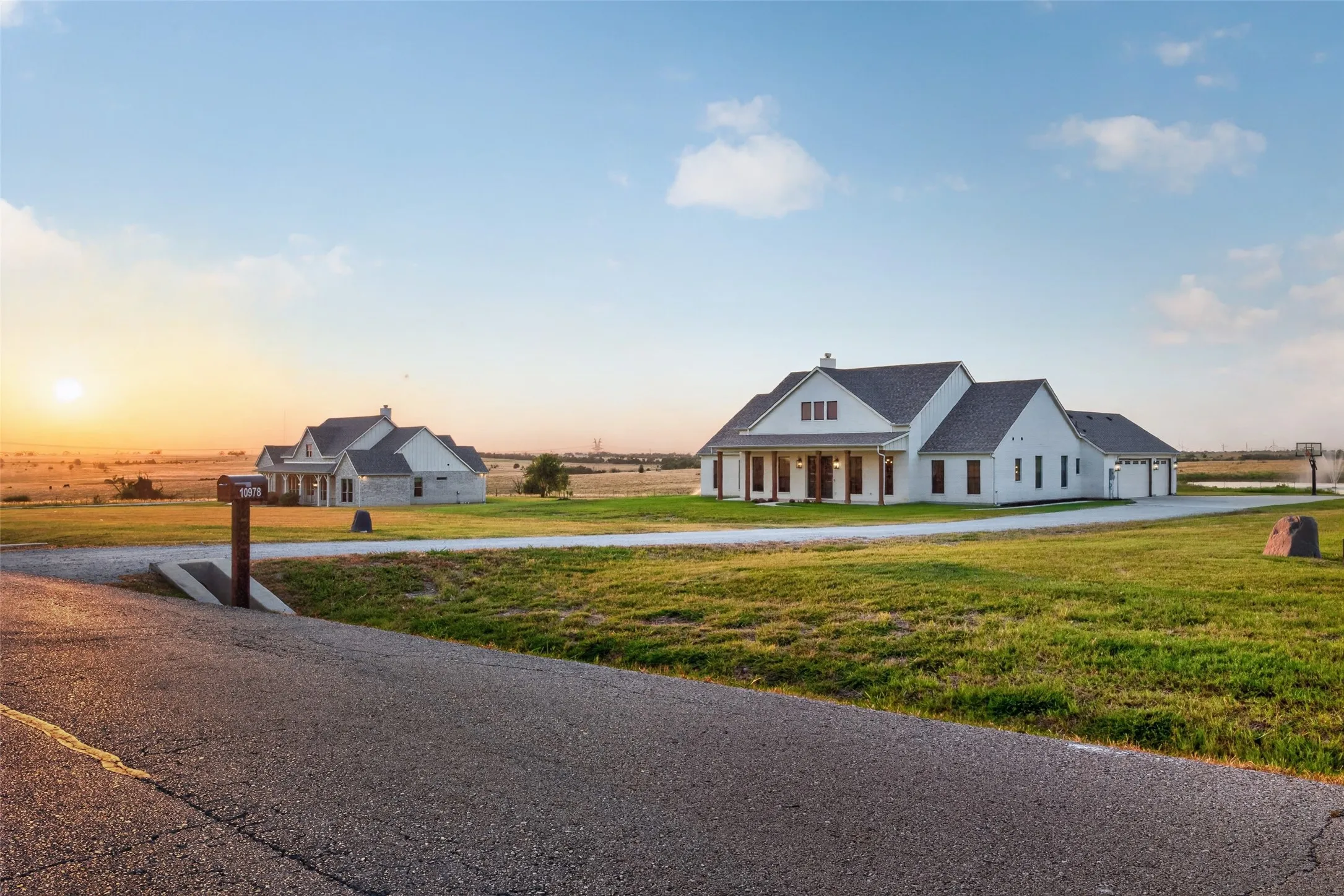 White siding exterior with a dark shingle roof, covered front porch, attached garage, and expansive green lawn