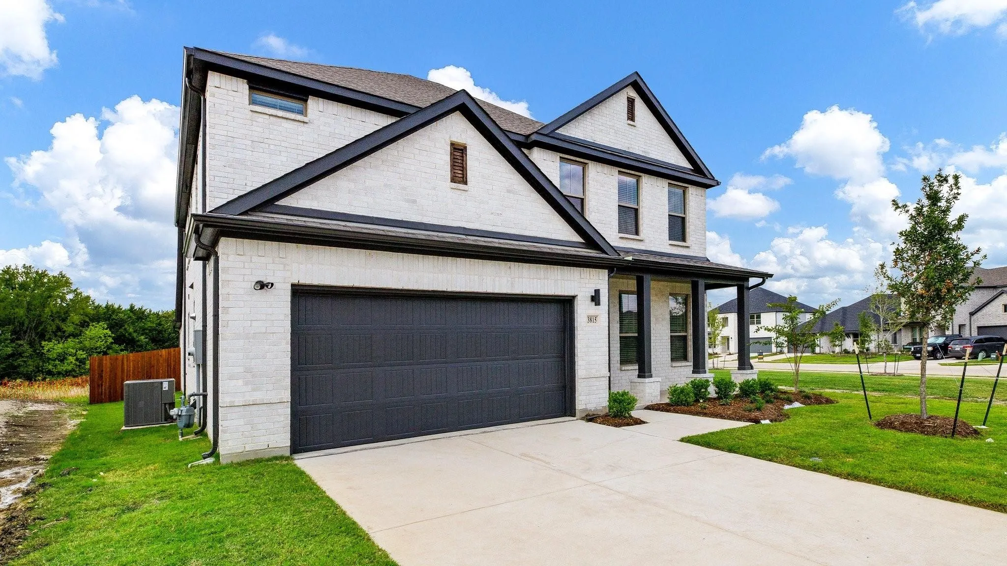 Modern two-story home featuring a crisp white exterior with black-trimmed gable roofline, dark charcoal garage doors, and a wide concrete driveway