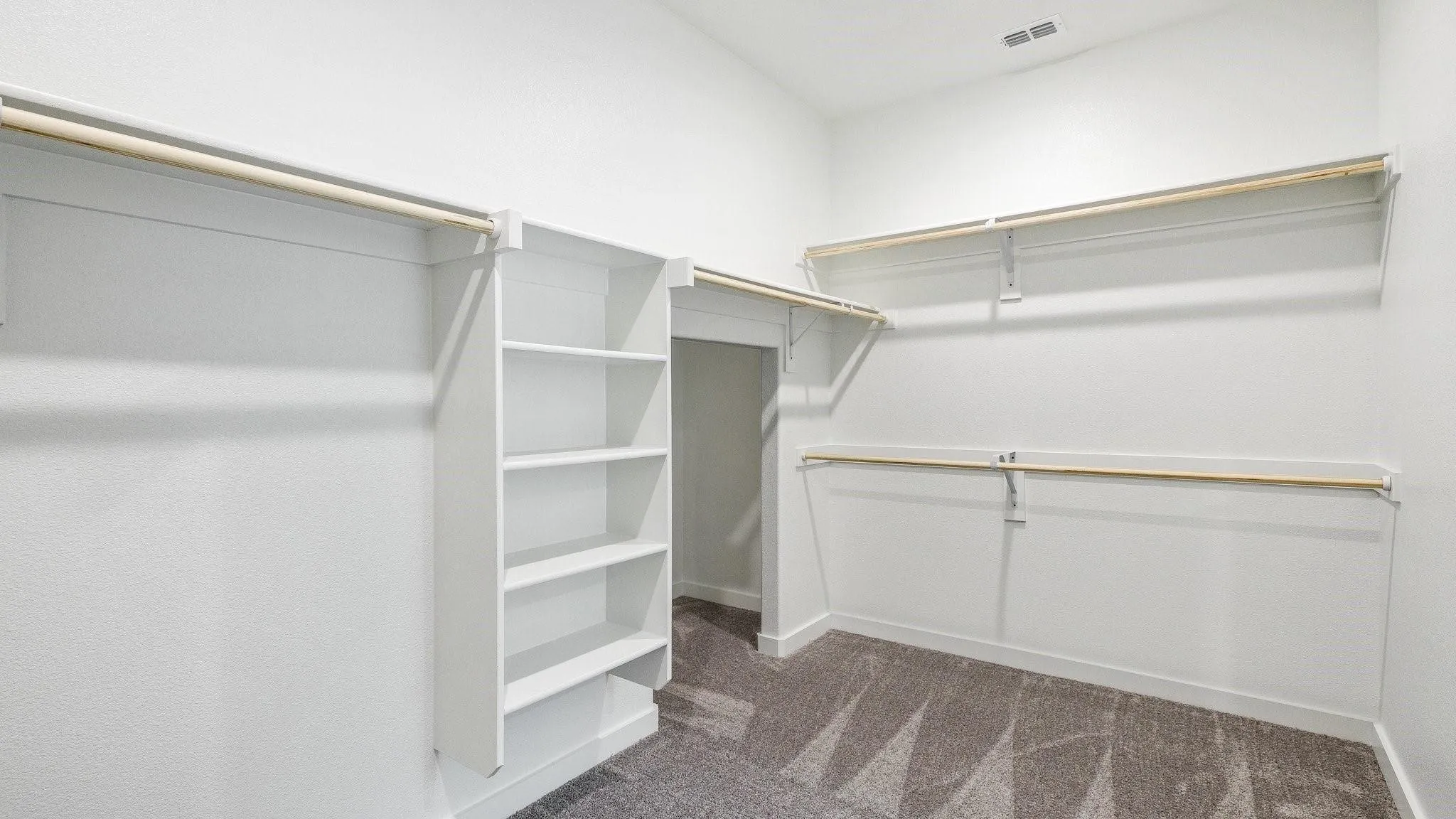 Spacious walk-in closet featuring built-in shelving, multiple hanging rods, and gray patterned carpeting
